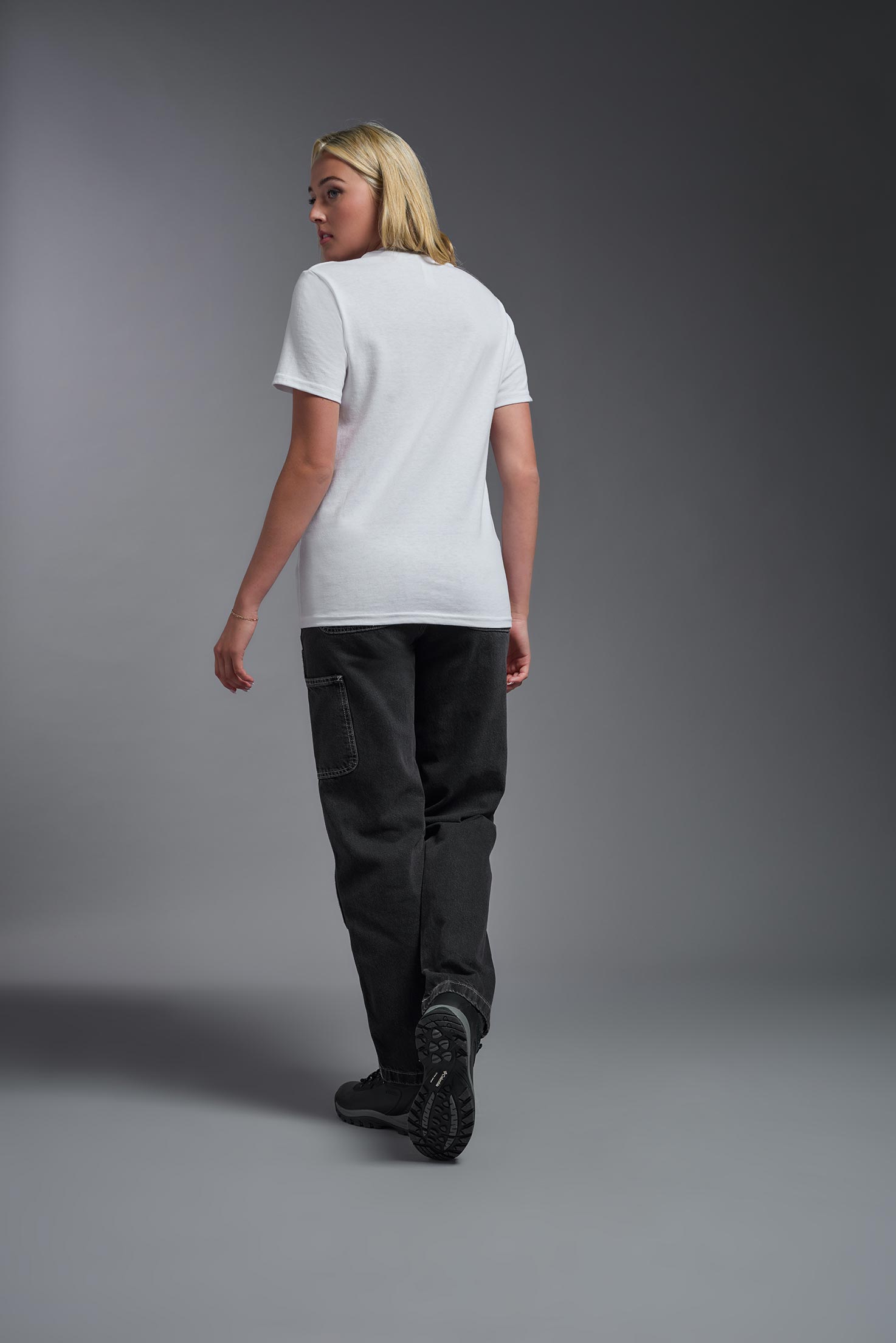 A female model wearing the unisex Imagen Short Sleeve Crewneck T-Shirt in the color white, made from 50% U.S. Grown Regenerative Cotton and 50% Recycled Polyester, showing the Relaxed Fit from a back view. This sustainable shirt is Made in the USA. #white