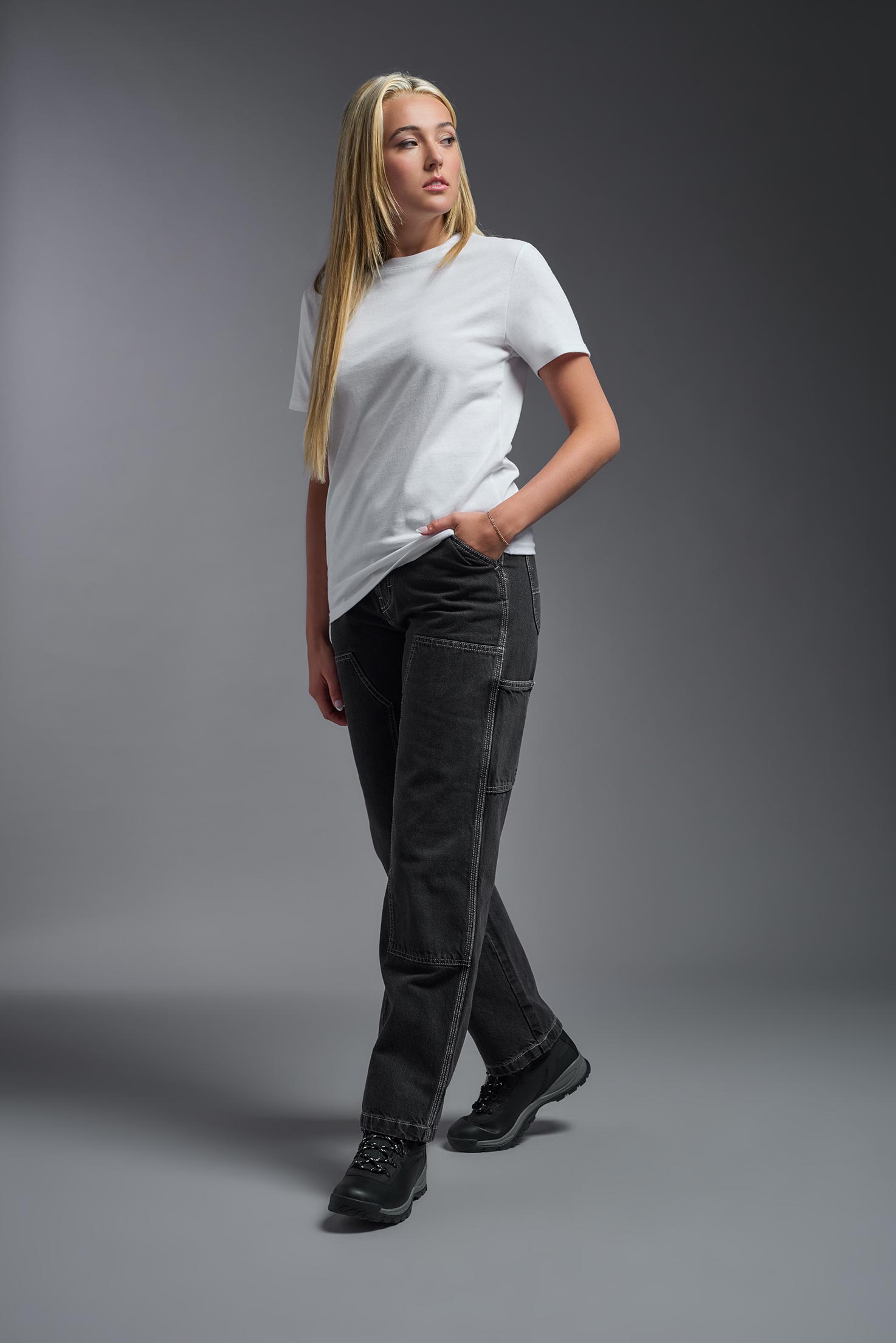 A female model wearing the unisex Imagen Short Sleeve Crewneck T-Shirt in the color white, made from 50% U.S. Grown Regenerative Cotton and 50% Recycled Polyester, showing the Relaxed Fit from a side view. This sustainable shirt is Made in the USA. #white