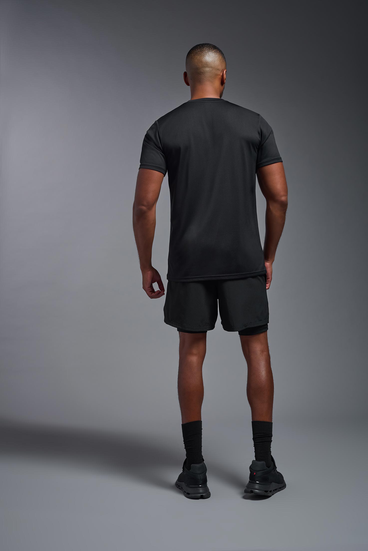 A male model wearing the men's EcoTek™ Recycled Performance Tee in the color black, made out of 100% recycled polyester REPREVE®, showing the modern fit from a back view. This shirt features a mechanical stretch, quick-dries, wicks moisture and is made in the USA. #black