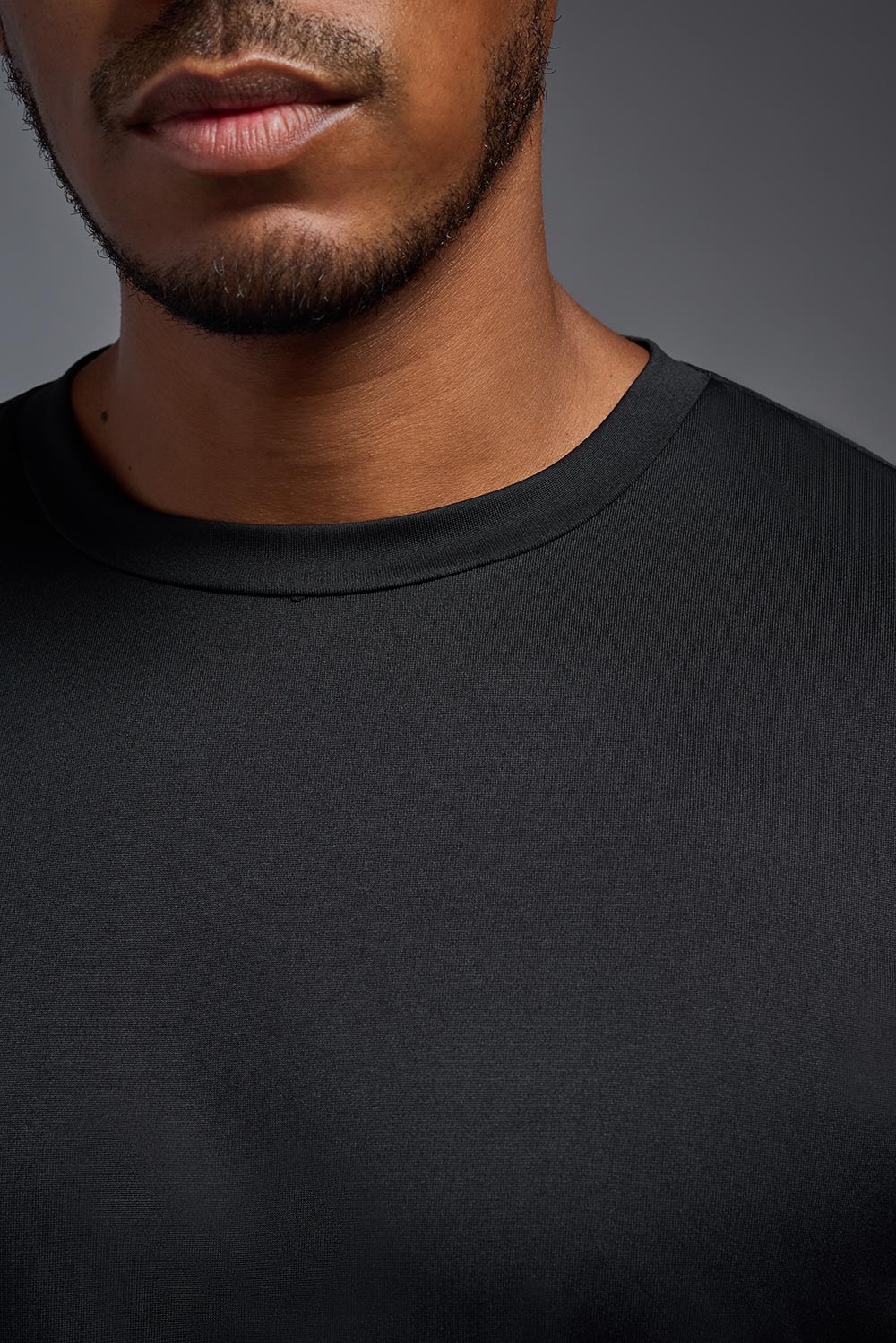A male model wearing the men's EcoTek™ Recycled Performance Tee in the color black, made out of 100% recycled polyester REPREVE®, showing the modern fit from a collar close-up view. This shirt features a mechanical stretch, quick-dries, wicks moisture and is made in the USA. #black