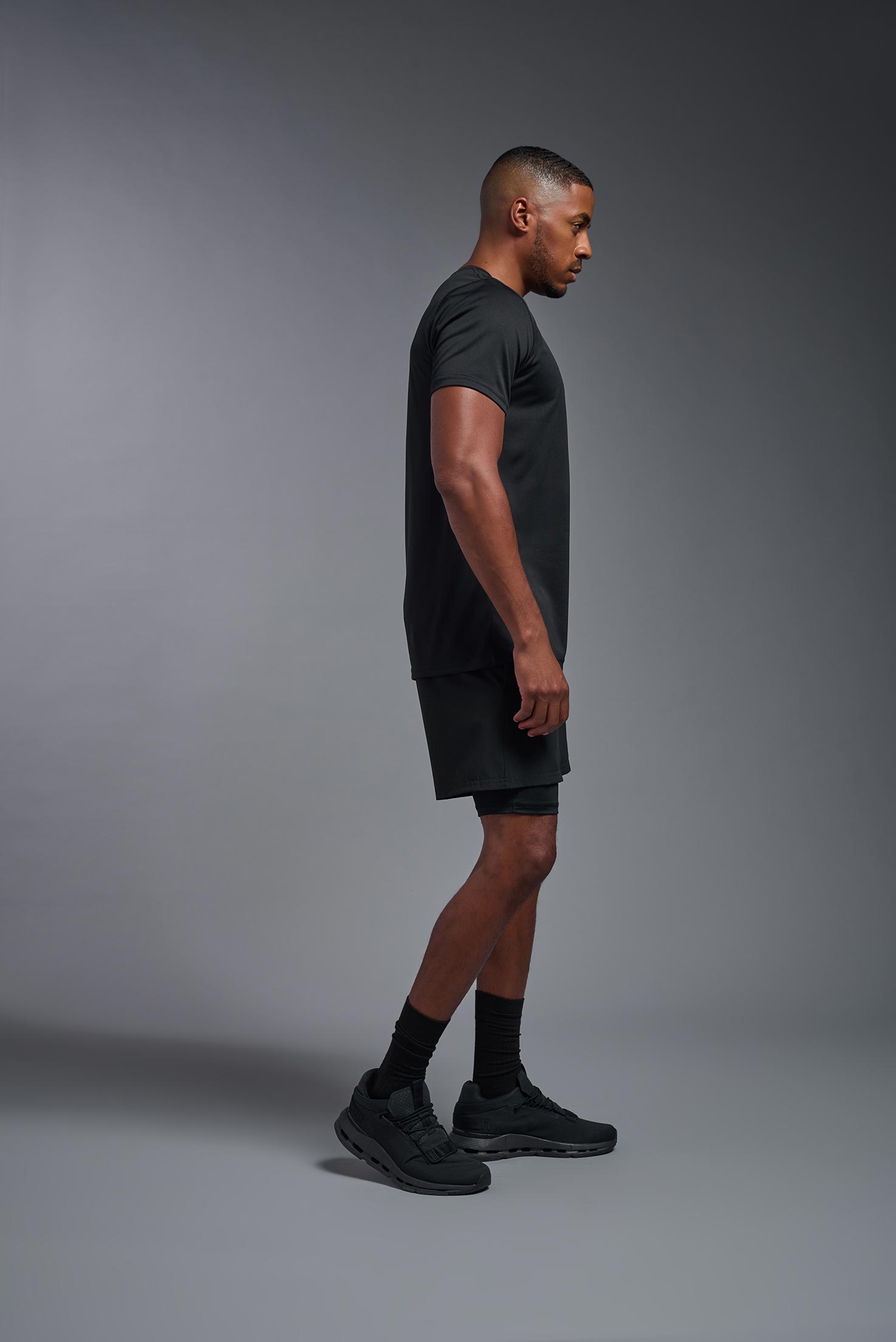 A male model wearing the men's EcoTek™ Recycled Performance Tee in the color black, made out of 100% recycled polyester REPREVE®, showing the modern fit from a side view. This shirt features a mechanical stretch, quick-dries, wicks moisture and is made in the USA. #black