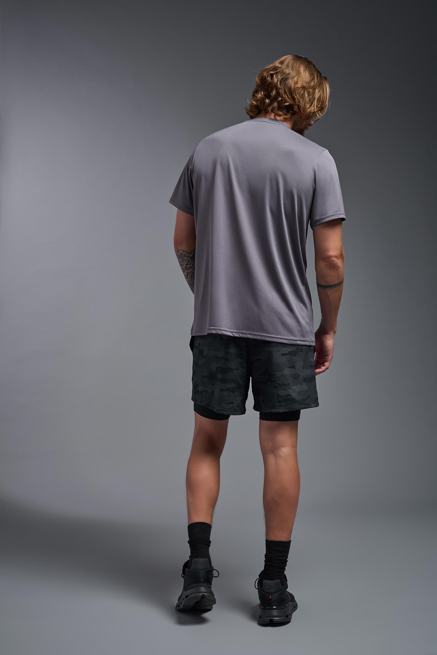 A male model wearing the men's EcoTek™ Recycled Performance Tee in the color charcoal, made out of 100% recycled polyester REPREVE®, showing the modern fit from a back view. This shirt features a mechanical stretch, quick-dries, wicks moisture and is made in the USA. #charcoal
