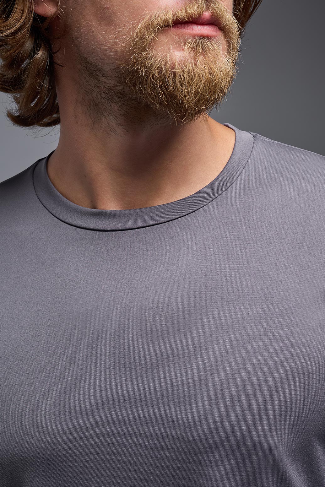 A male model wearing the men's EcoTek™ Recycled Performance Tee in the color charcoal, made out of 100% recycled polyester REPREVE®, showing the modern fit from a collar view. This shirt features a mechanical stretch, quick-dries, wicks moisture and is made in the USA. #charcoal