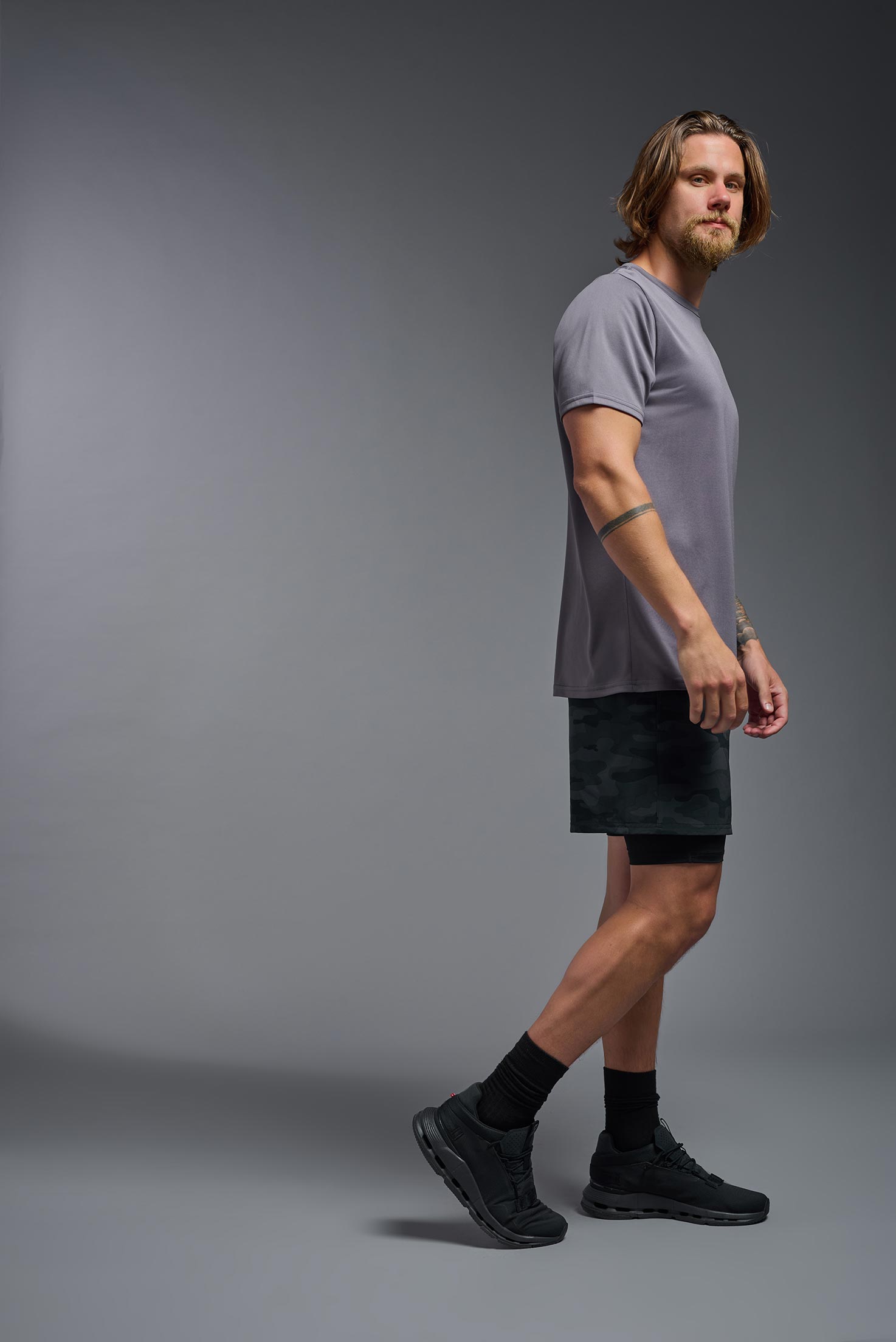 A male model wearing the men's EcoTek™ Recycled Performance Tee in the color charcoal, made out of 100% recycled polyester REPREVE®, showing the modern fit from a side view. This shirt features a mechanical stretch, quick-dries, wicks moisture and is made in the USA. #charcoal