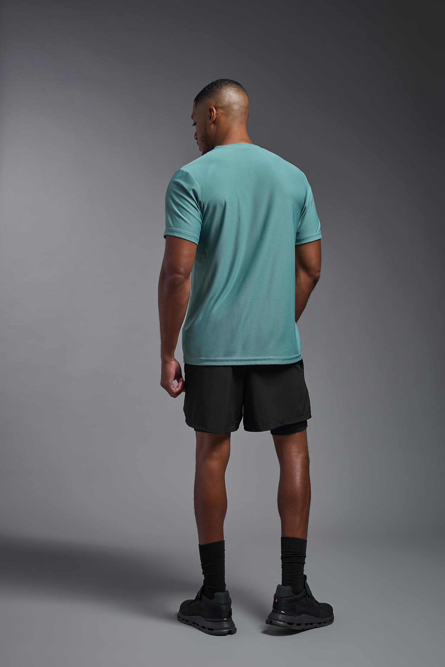 A male model wearing the men's EcoTek™ Recycled Performance Tee in the color juniper, made out of 100% recycled polyester REPREVE®, showing the modern fit from a back view. This shirt features a mechanical stretch, quick-dries, wicks moisture and is made in the USA. #juniper