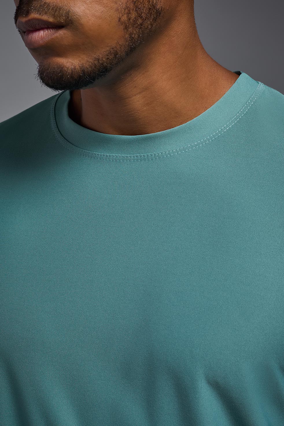 A male model wearing the men's EcoTek™ Recycled Performance Tee in the color juniper, made out of 100% recycled polyester REPREVE®, showing the modern fit from a collar view. This shirt features a mechanical stretch, quick-dries, wicks moisture and is made in the USA. #juniper