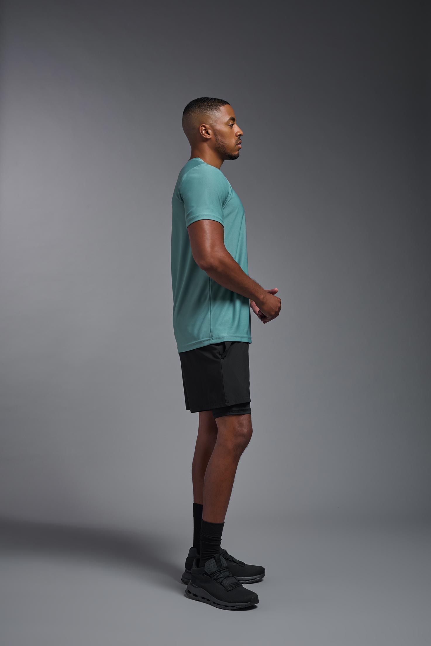 A male model wearing the men's EcoTek™ Recycled Performance Tee in the color juniper, made out of 100% recycled polyester REPREVE®, showing the modern fit from a side view. This shirt features a mechanical stretch, quick-dries, wicks moisture and is made in the USA. #juniper