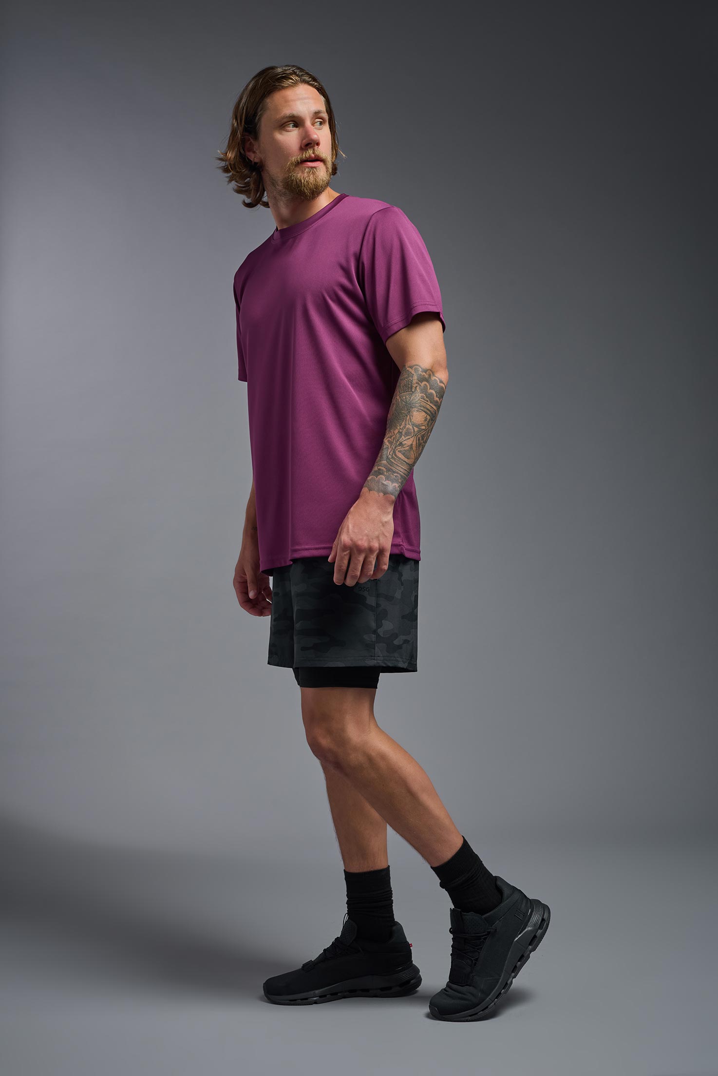 A male model wearing the men's EcoTek™ Recycled Performance Tee in the color merlot, made out of 100% recycled polyester REPREVE®, showing the modern fit from a side view. This shirt features a mechanical stretch, quick-dries, wicks moisture and is made in the USA. #merlot