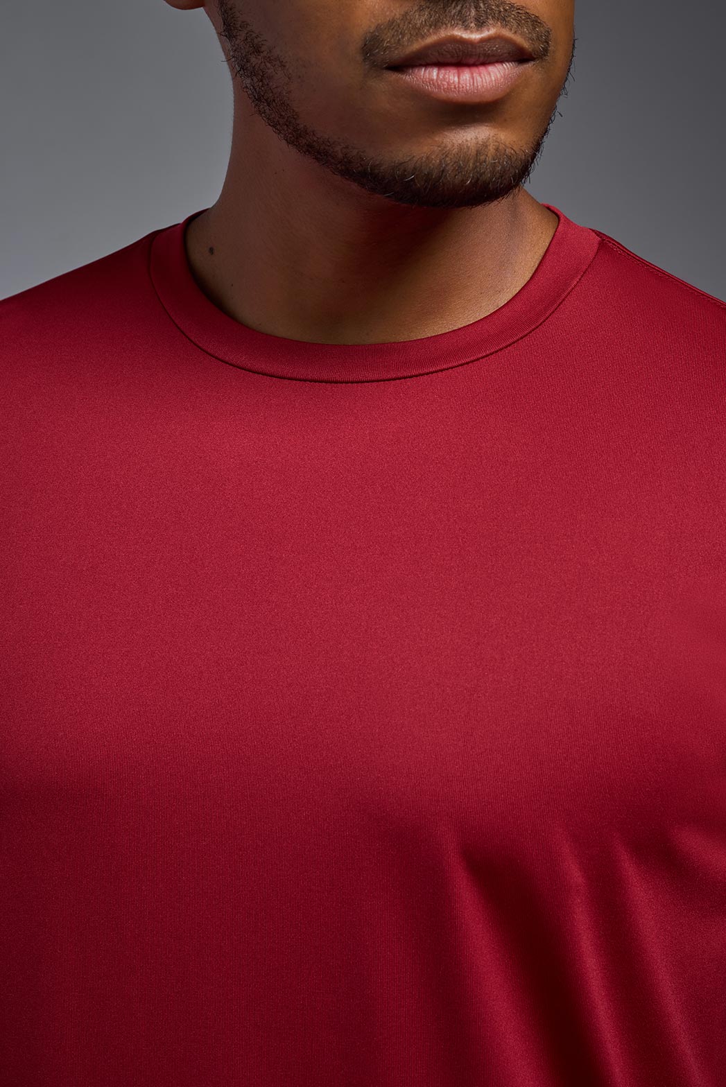 A male model wearing the men's EcoTek™ Recycled Performance Tee in the color poinsettia, made out of 100% recycled polyester REPREVE®, showing the modern fit from a close-up collar view. This shirt features a mechanical stretch, quick-dries, wicks moisture and is made in the USA. #poinsettia