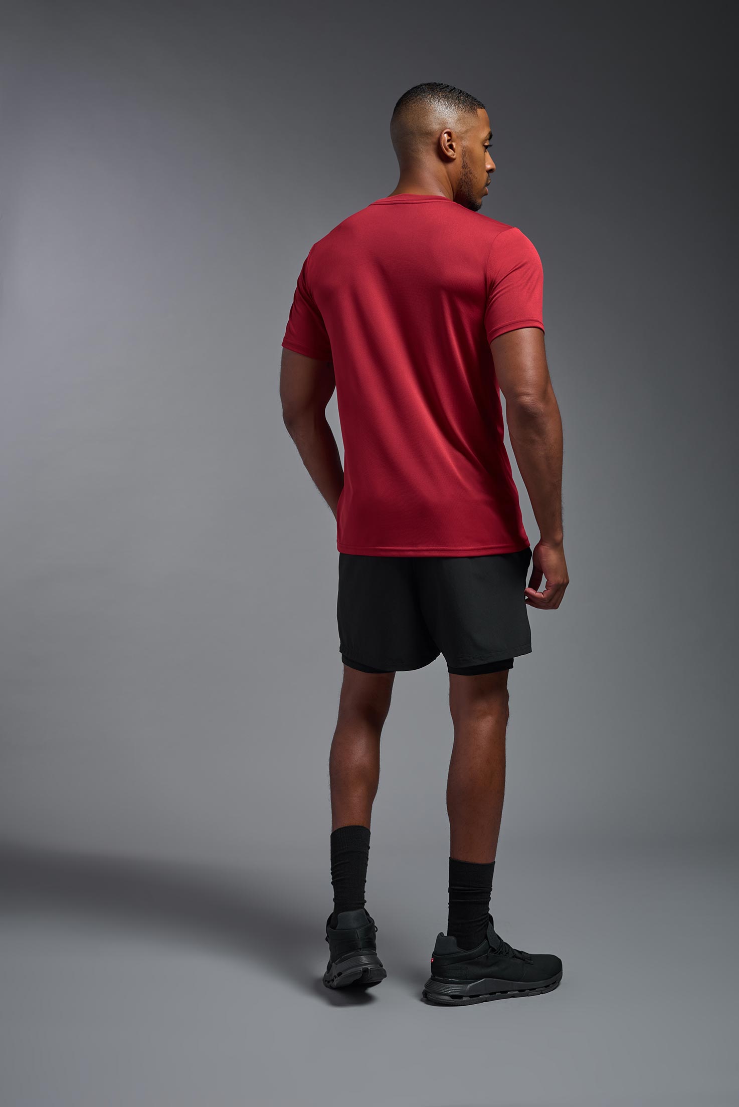 A male model wearing the men's EcoTek™ Recycled Performance Tee in the color poinsettia, made out of 100% recycled polyester REPREVE®, showing the modern fit from a back view. This shirt features a mechanical stretch, quick-dries, wicks moisture and is made in the USA. #poinsettia