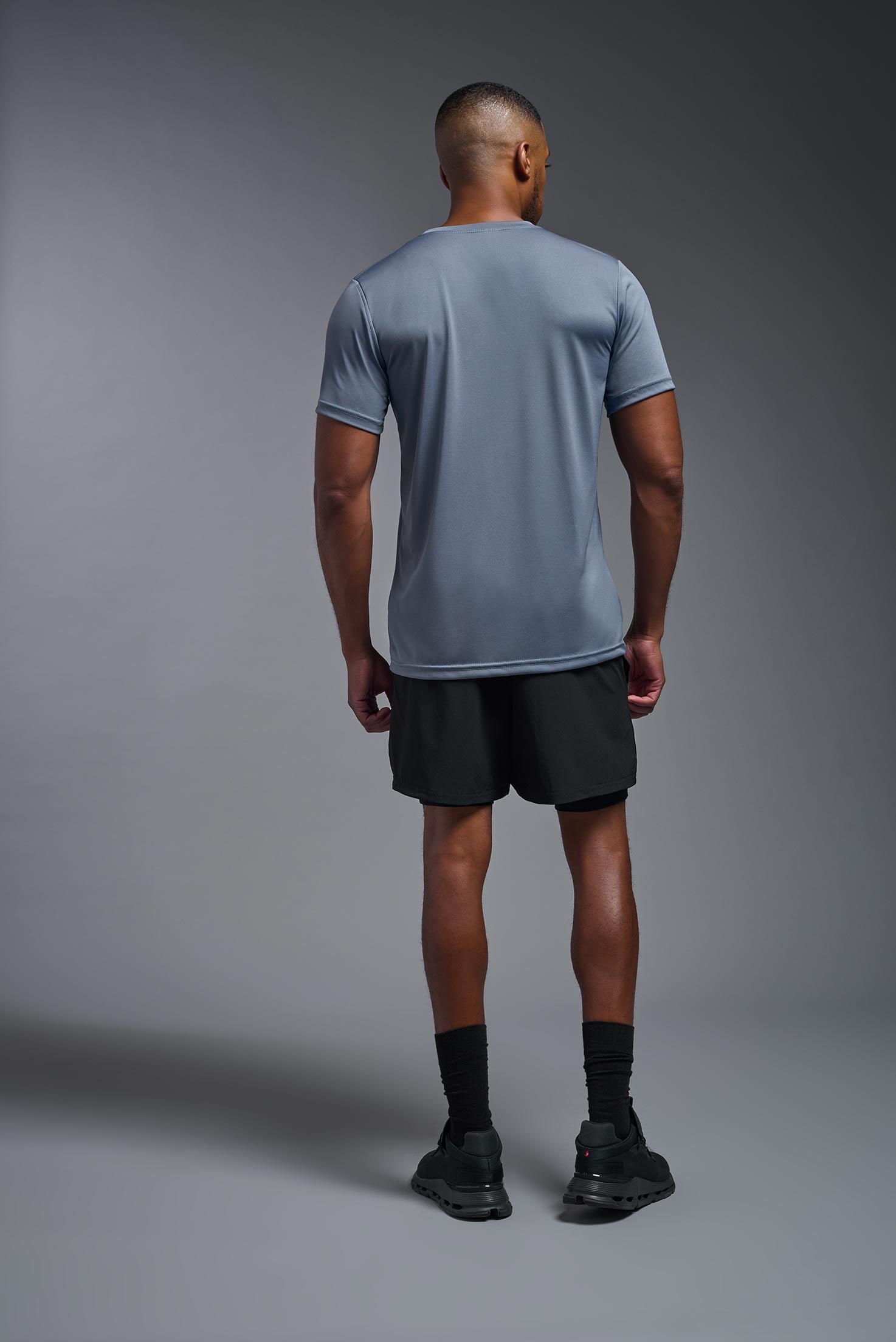 A male model wearing the men's EcoTek™ Recycled Performance Tee in the color tahoe, made out of 100% recycled polyester REPREVE®, showing the modern fit from a back view. This shirt features a mechanical stretch, quick-dries, wicks moisture and is made in the USA. #tahoe