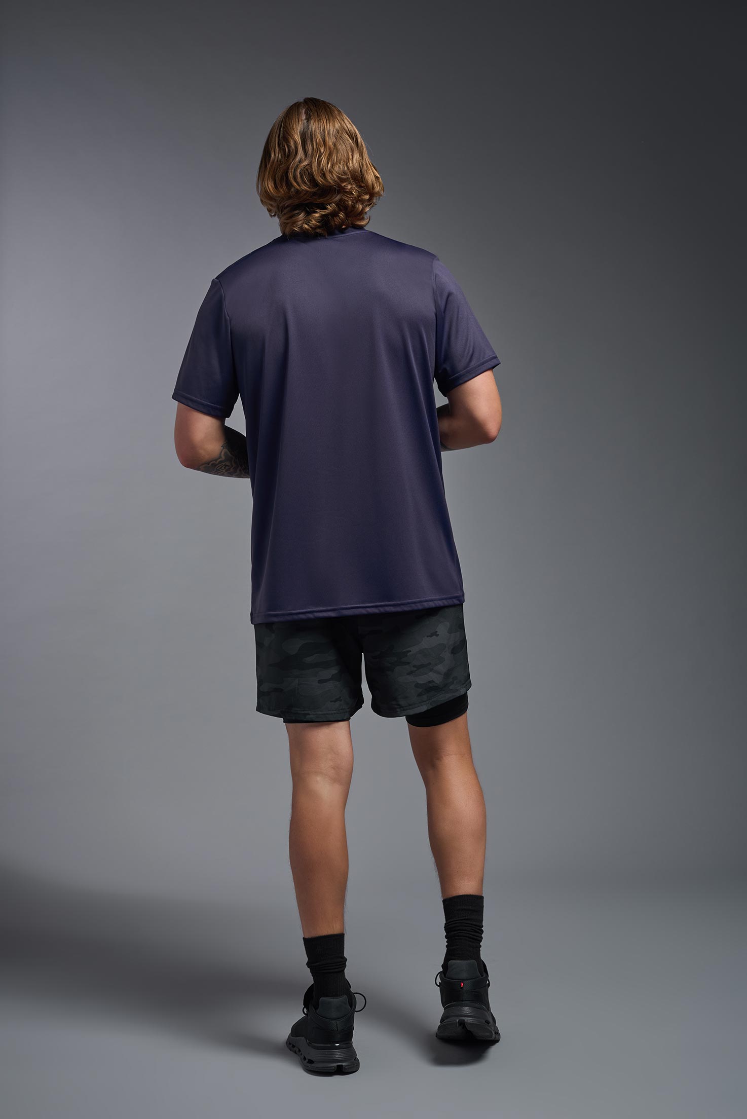 A male model wearing the men's EcoTek™ Recycled Performance Tee in the color twilight, made out of 100% recycled polyester REPREVE®, showing the modern fit from a back view. This shirt features a mechanical stretch, quick-dries, wicks moisture and is made in the USA. #twilight