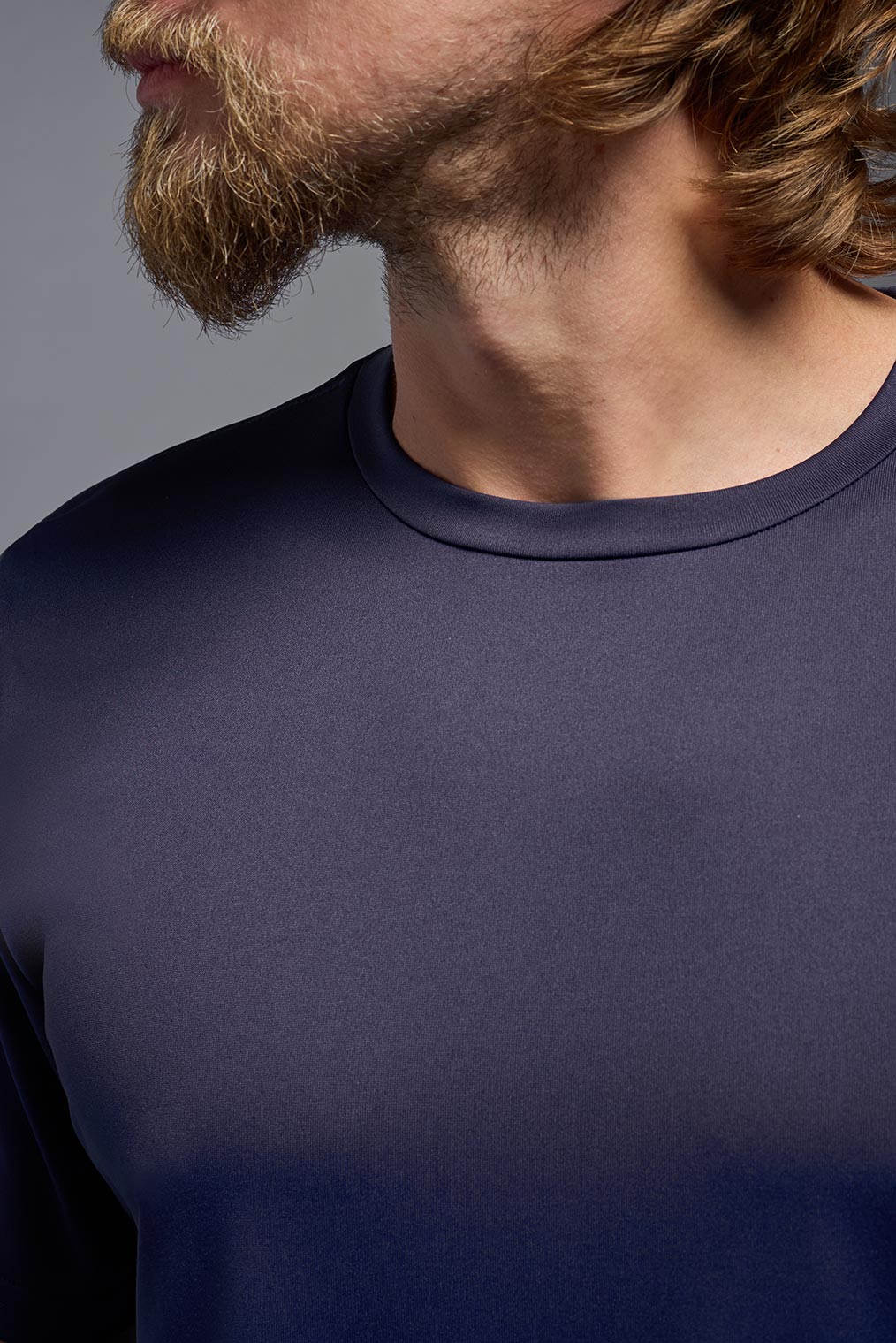 A male model wearing the men's EcoTek™ Recycled Performance Tee in the color twilight, made out of 100% recycled polyester REPREVE®, showing the modern fit from a collar close-up view. This shirt features a mechanical stretch, quick-dries, wicks moisture and is made in the USA. #twilight