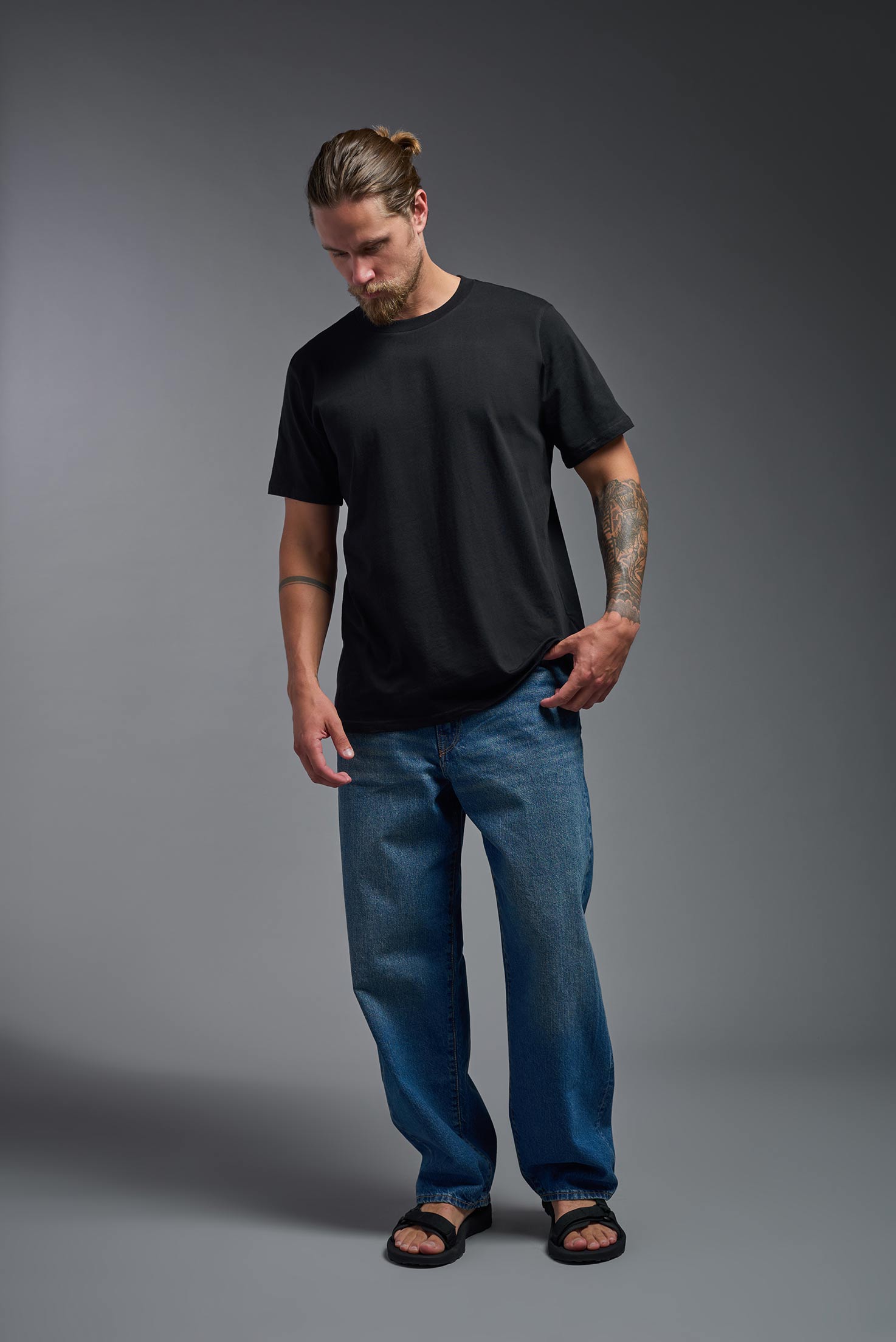 A male model wearing the unisex Organic Soft Cotton T-shirt in the color black, made in the USA from 100% GOTS certified organic cotton from a front view. This shirt is unisex, made in the USA, and perfect for screen printing and decorating. #black