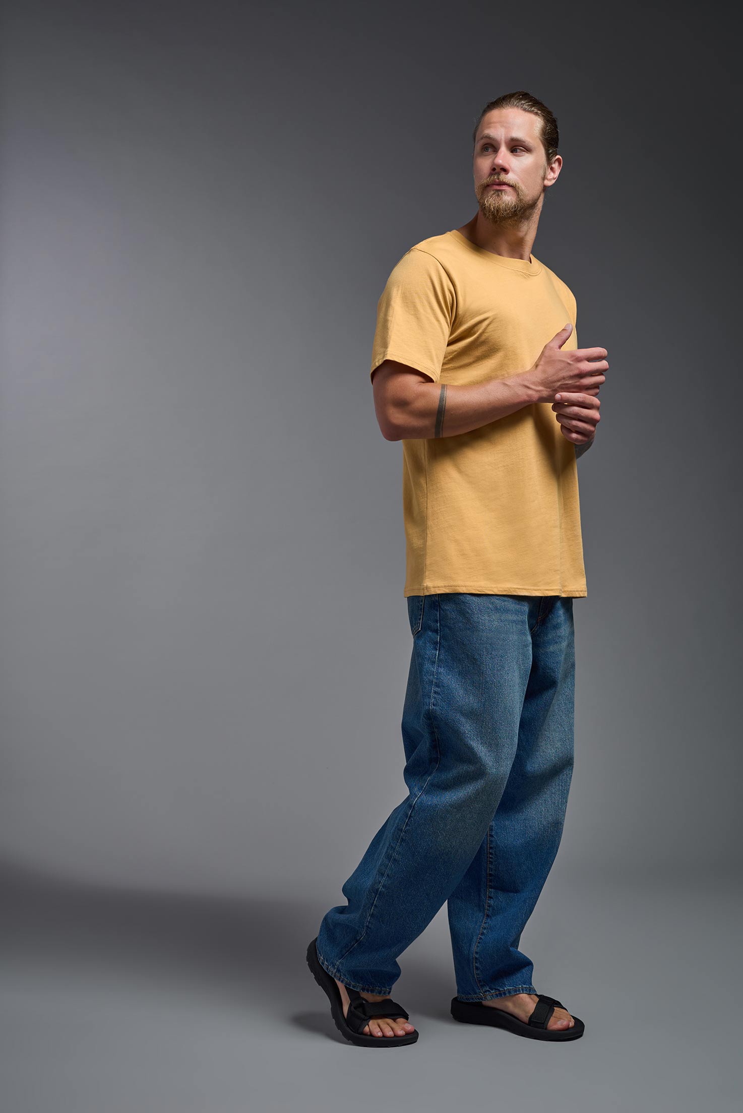 A male model wearing the unisex Organic Soft Cotton T-shirt in the color harvest, made in the USA from 100% GOTS certified organic cotton from a side view. This shirt is unisex, made in the USA, and perfect for bulk screen printing and decorating. #harvest