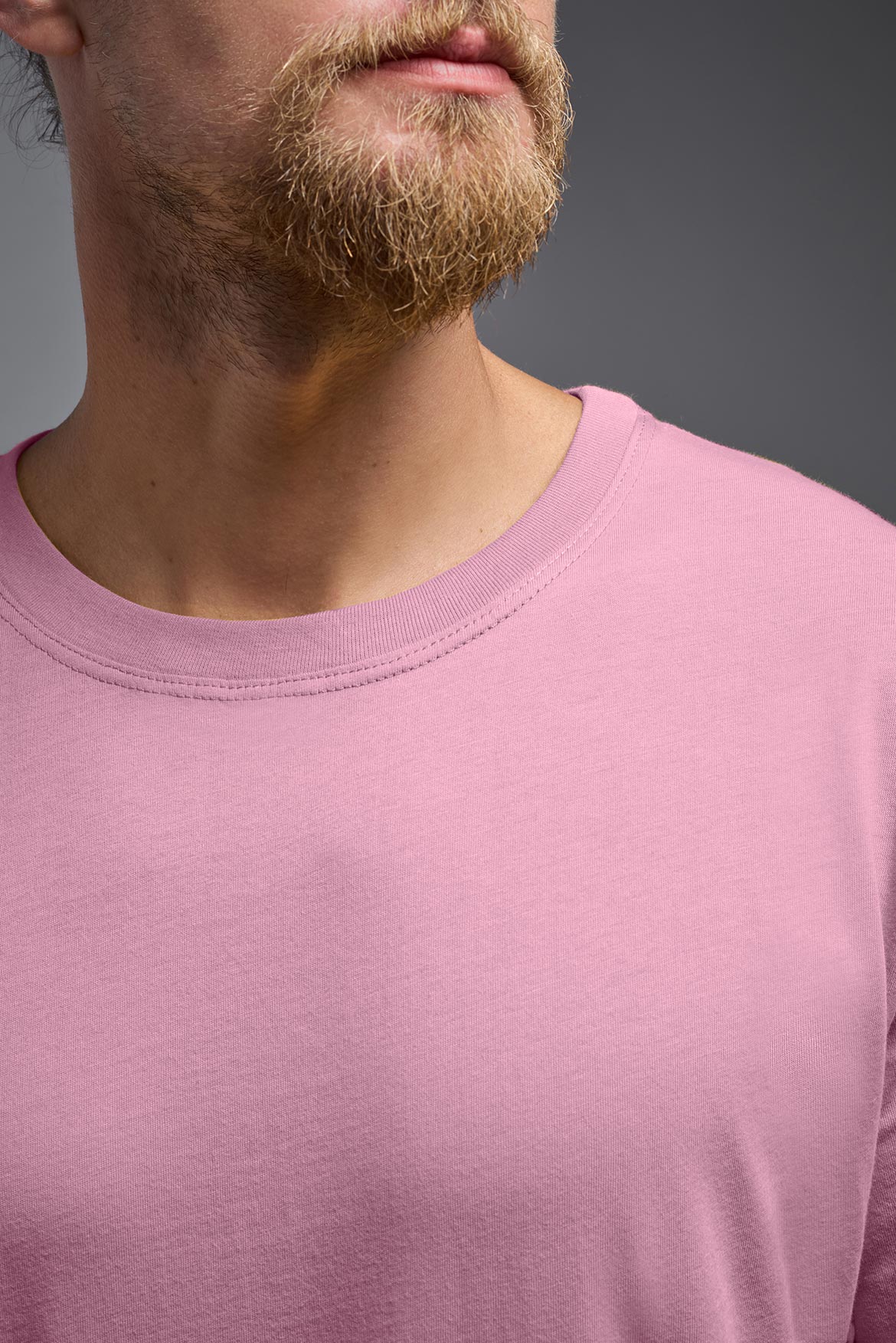 A male model wearing the unisex Organic Soft Cotton T-shirt in the color Himalayan salt pink, made in the USA from 100% GOTS certified organic cotton from a close up collar front view. This shirt is unisex, made in the USA, and perfect for bulk screen printing and decorating. #himalayan-salt