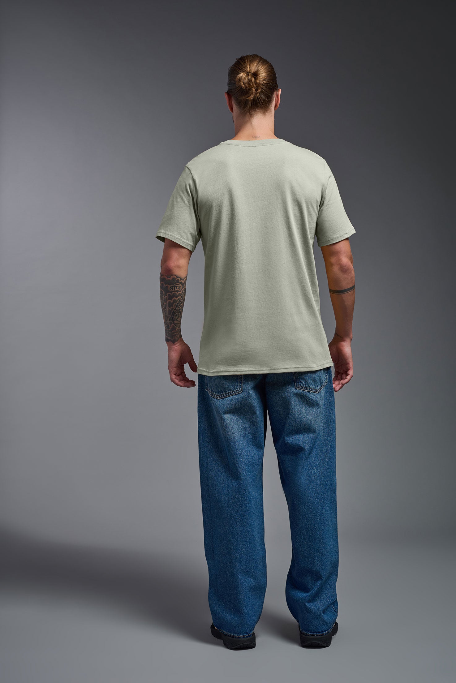 A male model wearing the unisex Organic Soft Cotton T-shirt in the color sage green, made in the USA from 100% GOTS certified organic cotton from a back view. This shirt is unisex, made in the USA, and perfect for bulk screen printing and decorating. #sage