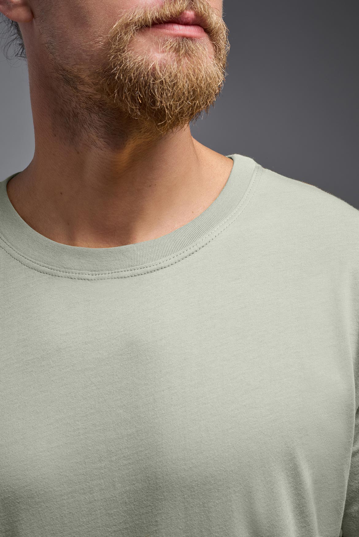 A male model wearing the unisex Organic Soft Cotton T-shirt in the color sage green, made in the USA from 100% GOTS certified organic cotton from a close up collar front view. This shirt is unisex, made in the USA, and perfect for bulk screen printing and decorating. #sage