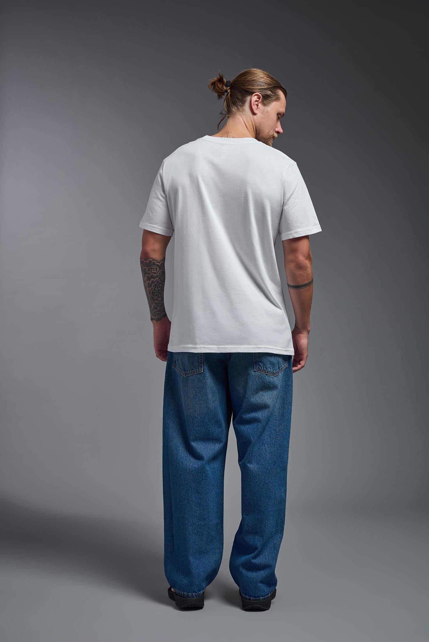 A male model wearing the unisex Organic Soft Cotton T-shirt in the color white, made in the USA from 100% GOTS certified organic cotton from a back view. #white