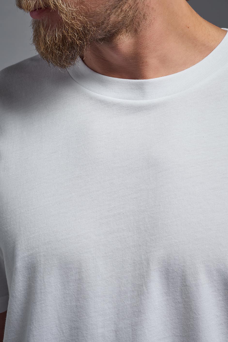 A male model wearing the unisex Organic Soft Cotton T-shirt in the color white, made in the USA from 100% GOTS certified organic cotton from a front close-up collar view. #white