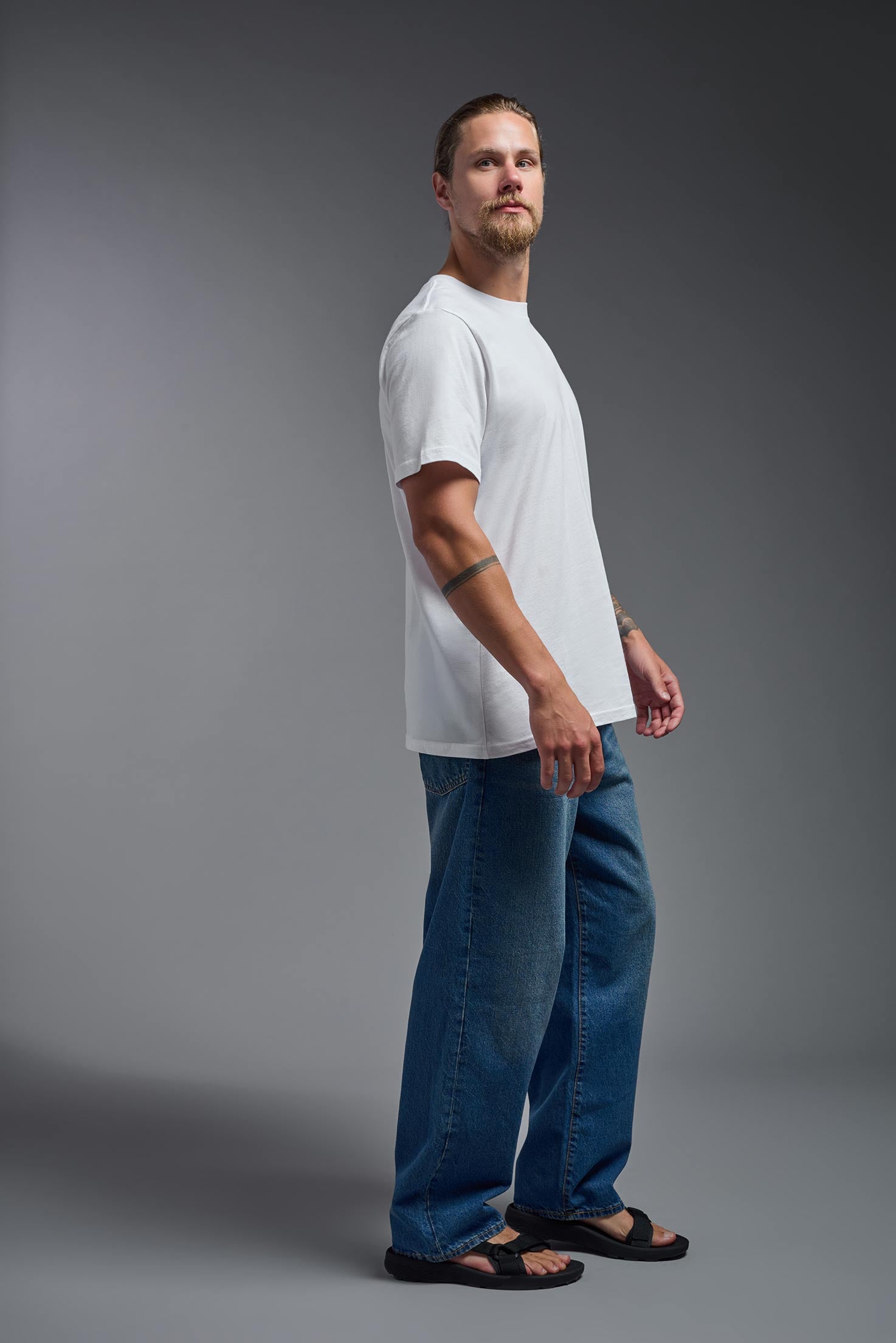 A male model wearing the unisex Organic Soft Cotton T-shirt in the color white, made in the USA from 100% GOTS certified organic cotton from a side view. #white