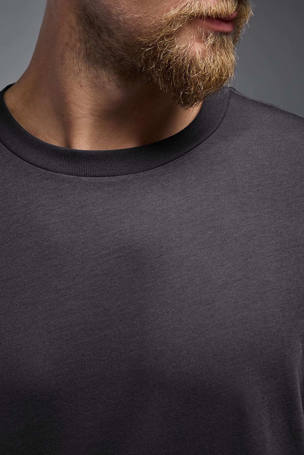 A male model wearing the unisex Organic Soft Cotton T-shirt in the color carbon, made from 100% GOTS certified organic cotton from a closeup collar front view. This shirt is unisex, made in the USA, and perfect for bulk screen printing and decorating. #carbon