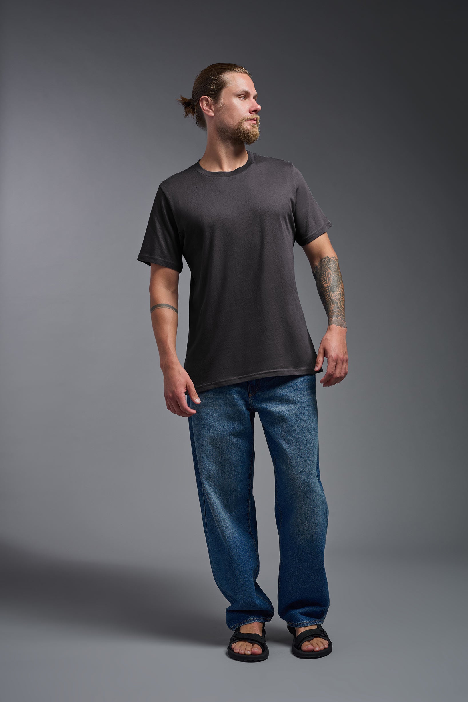 A male model wearing the unisex Organic Soft Cotton T-shirt in the color carbon, made from 100% GOTS certified organic cotton from a full body front view. This shirt is unisex, made in the USA, and perfect for bulk screen printing and decorating. #carbon