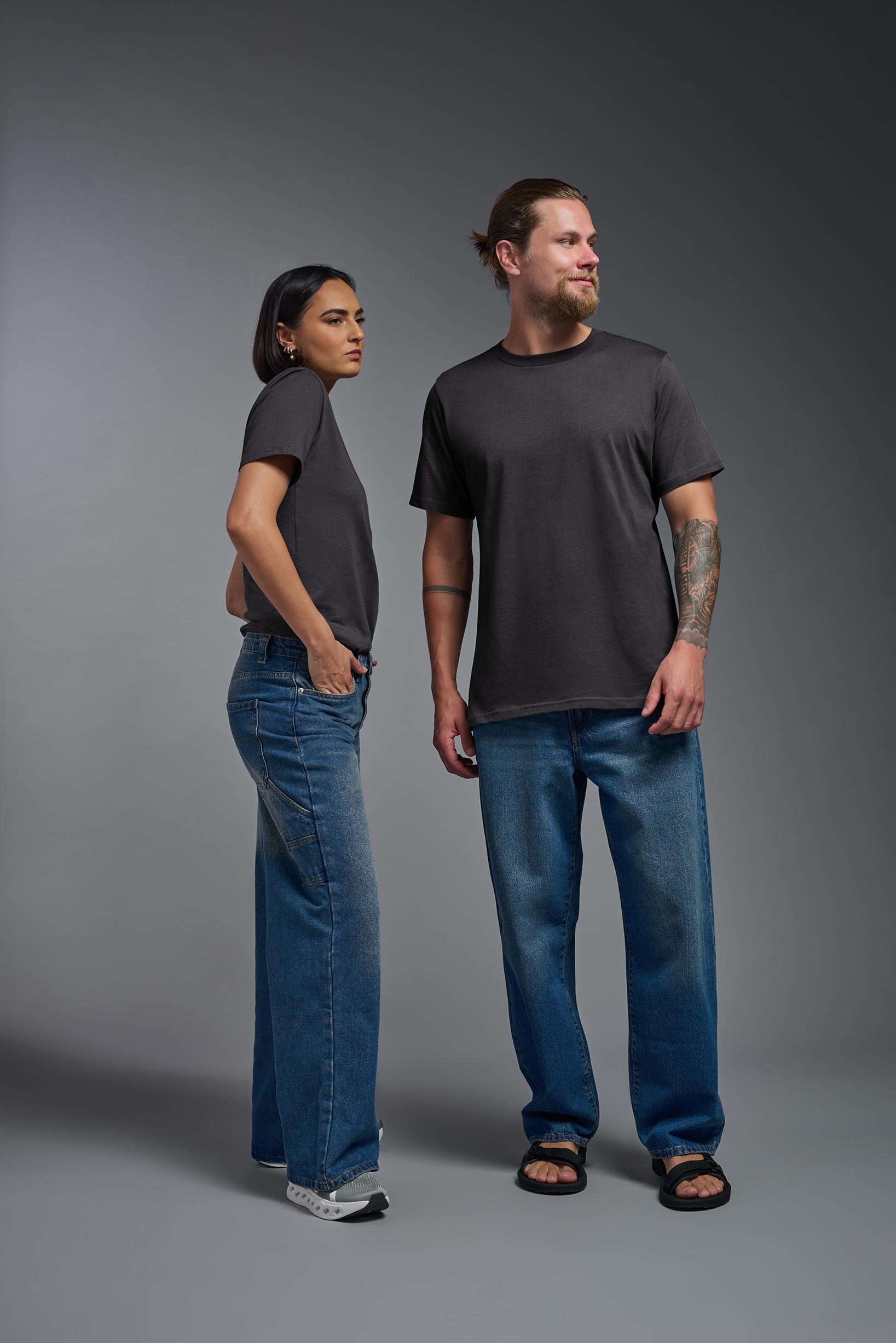 A male and female model wearing the unisex Organic Soft Cotton T-shirt in the color carbon, made from 100% GOTS certified organic cotton from a full body front view. This shirt is unisex, made in the USA, and perfect for bulk screen printing and decorating. #carbon