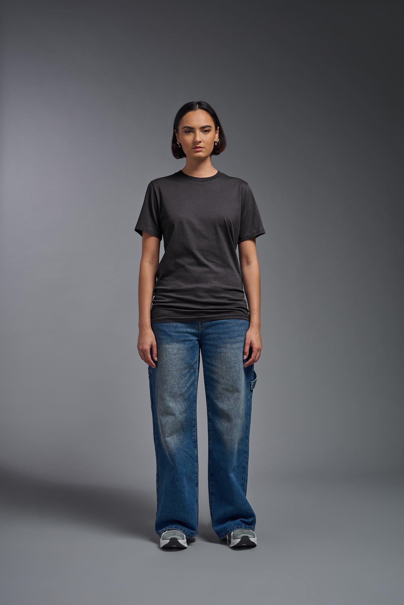 A female model wearing the unisex Organic Soft Cotton T-shirt in the color carbon, made from 100% GOTS certified organic cotton from a full body front view. This shirt is unisex, made in the USA, and perfect for bulk screen printing and decorating. #carbon