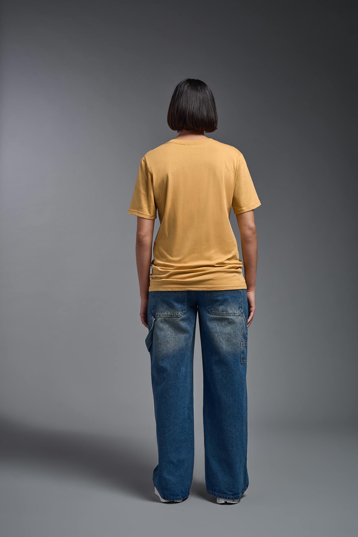 A female model wearing the unisex Organic Soft Cotton T-shirt in the color harvest, made in the USA from 100% GOTS certified organic cotton from a back view. This shirt is unisex, made in the USA, and perfect for bulk screen printing and decorating. #harvest