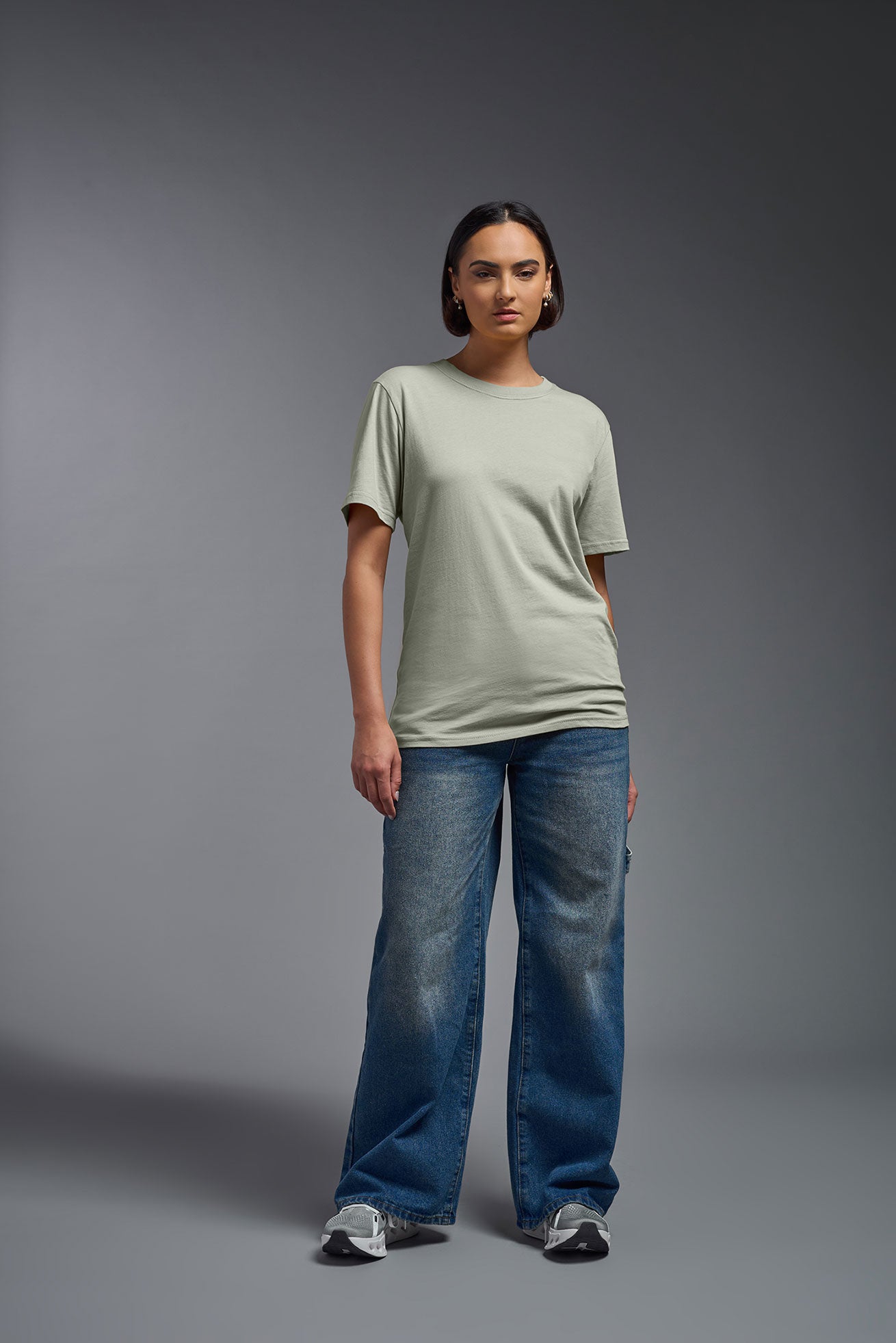 A female model wearing the unisex Organic Soft Cotton T-shirt in the color sage green, made in the USA from 100% GOTS certified organic cotton from a front view. This shirt is unisex, made in the USA, and perfect for bulk screen printing and decorating. #sage