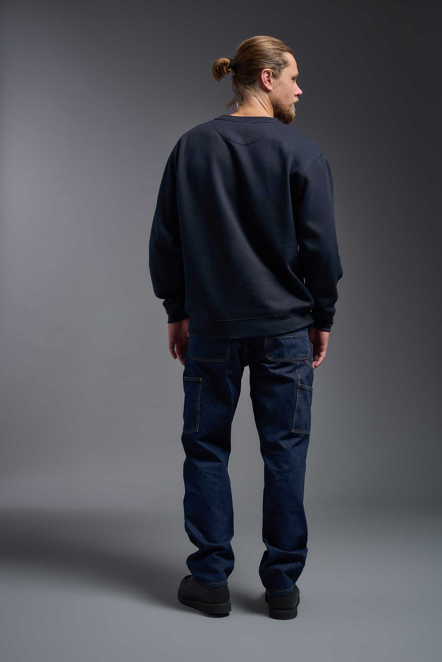 A male model wearing the unisex Americana 3-End Fleece Crewneck Sweatshirt in the color navy, made from 75% combed ring-spun USA-grown cotton and 25% polyester, showing the relaxed fit from a close-up back view. This premium fleece hoodie is Made in the USA. #navy