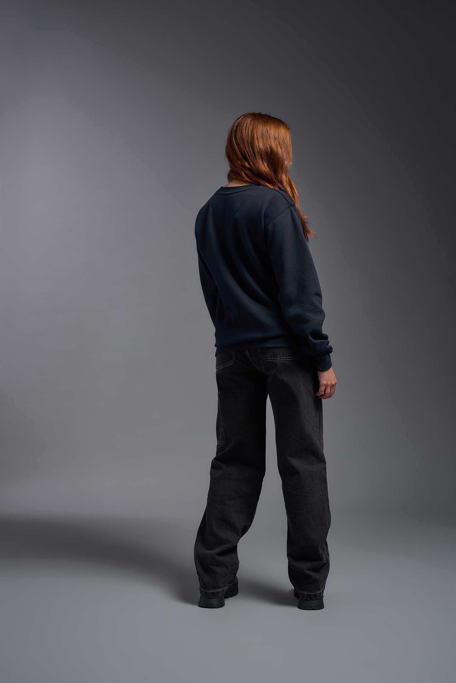 A female model wearing the unisex Americana 3-End Fleece Crewneck Sweatshirt in the color navy, made from 75% combed ring-spun USA-grown cotton and 25% polyester, showing the relaxed fit from a back view. This premium fleece hoodie is Made in the USA. #navy
