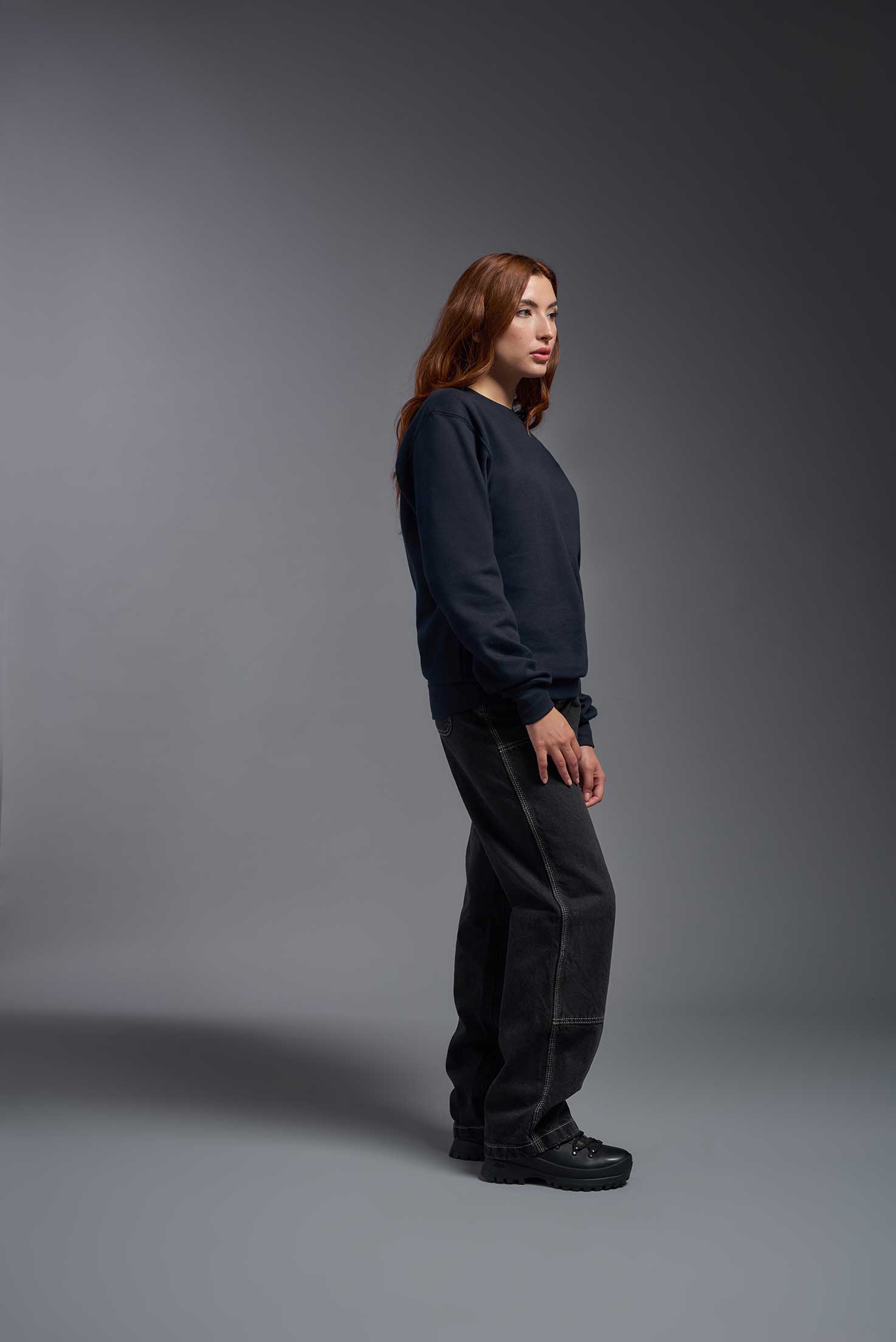 A female model wearing the unisex Americana 3-End Fleece Crewneck Sweatshirt in the color navy, made from 75% combed ring-spun USA-grown cotton and 25% polyester, showing the relaxed fit from a side view. This premium fleece hoodie is Made in the USA. #navy