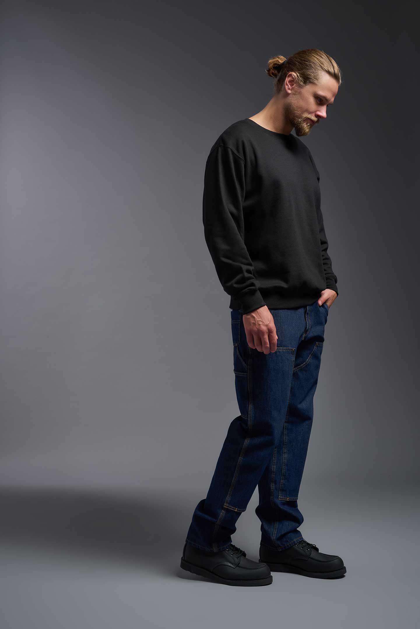 A male model wearing the unisex Americana 3-End Fleece Crewneck Sweatshirt in the color black, made from 75% combed ring-spun USA-grown cotton and 25% polyester, showing the relaxed fit from a side view. This premium fleece hoodie is Made in the USA. #black