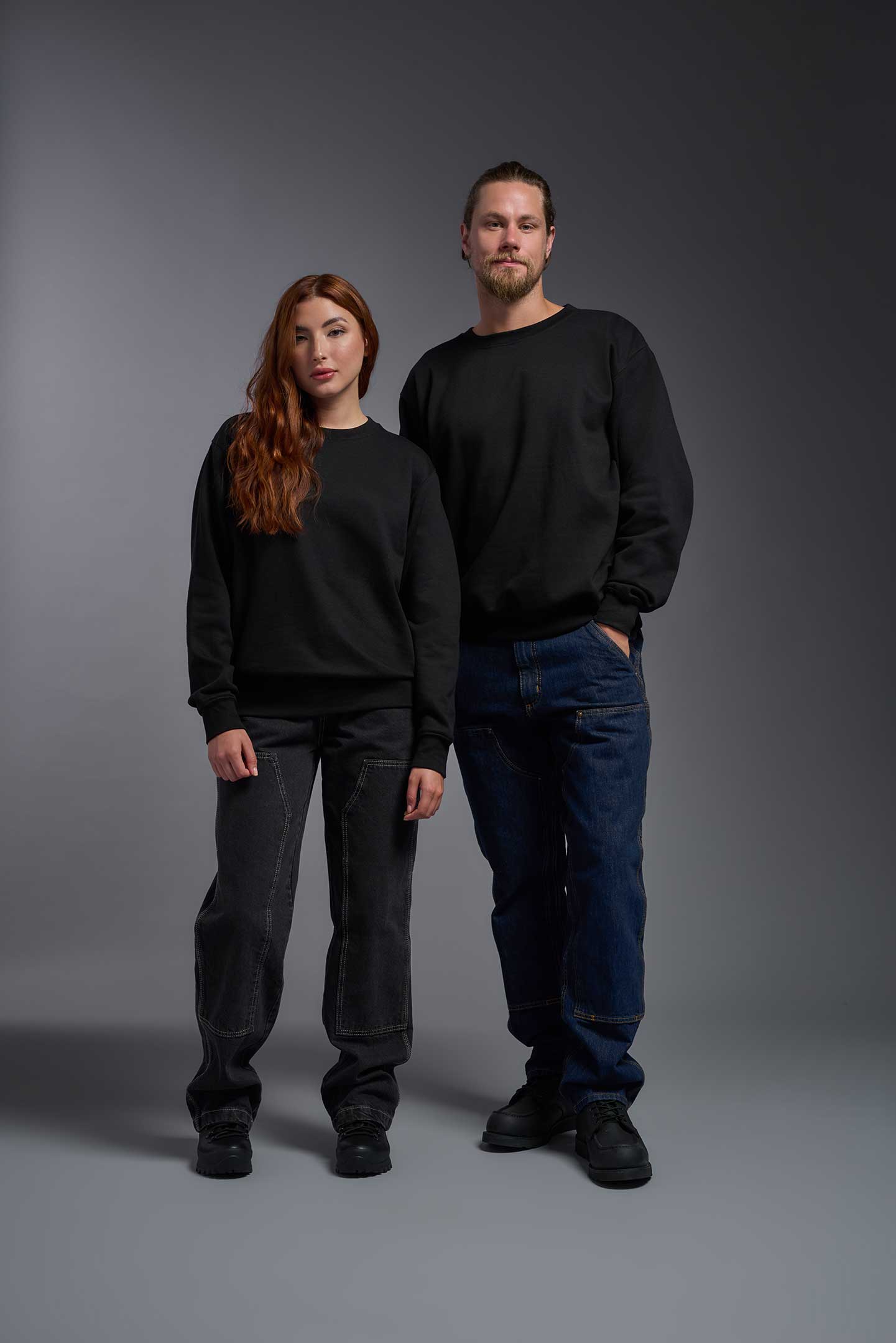 A male and female model wearing the unisex Americana 3-End Fleece Crewneck Sweatshirt in the color black, made from 75% combed ring-spun USA-grown cotton and 25% polyester, showing the relaxed fit from a front view. This premium fleece hoodie is Made in the USA. #black