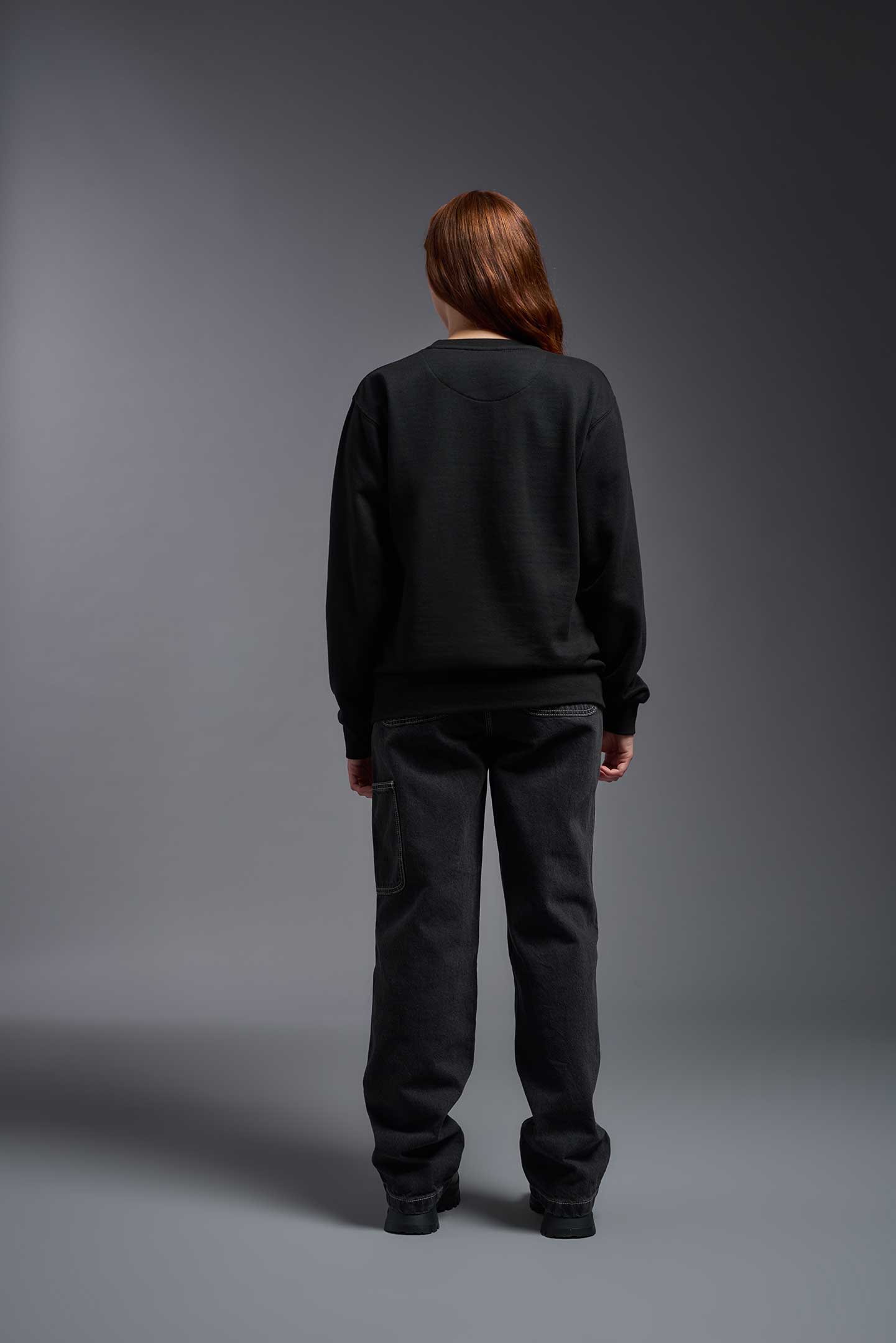 A female model wearing the unisex Americana 3-End Fleece Crewneck Sweatshirt in the color black, made from 75% combed ring-spun USA-grown cotton and 25% polyester, showing the relaxed fit from a back view. This premium fleece hoodie is Made in the USA. #black
