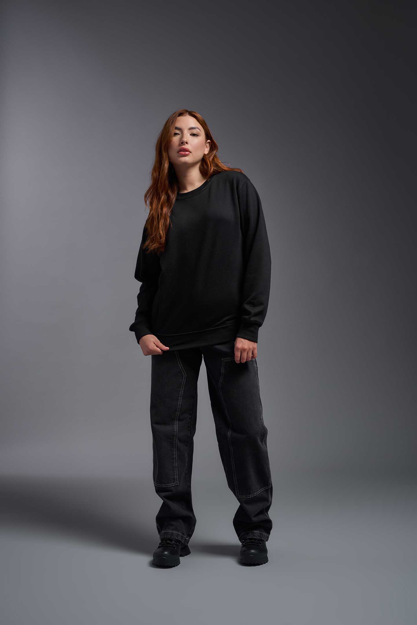 A female model wearing the unisex Americana 3-End Fleece Crewneck Sweatshirt in the color black, made from 75% combed ring-spun USA-grown cotton and 25% polyester, showing the relaxed fit from a front view. This premium fleece hoodie is Made in the USA. #black