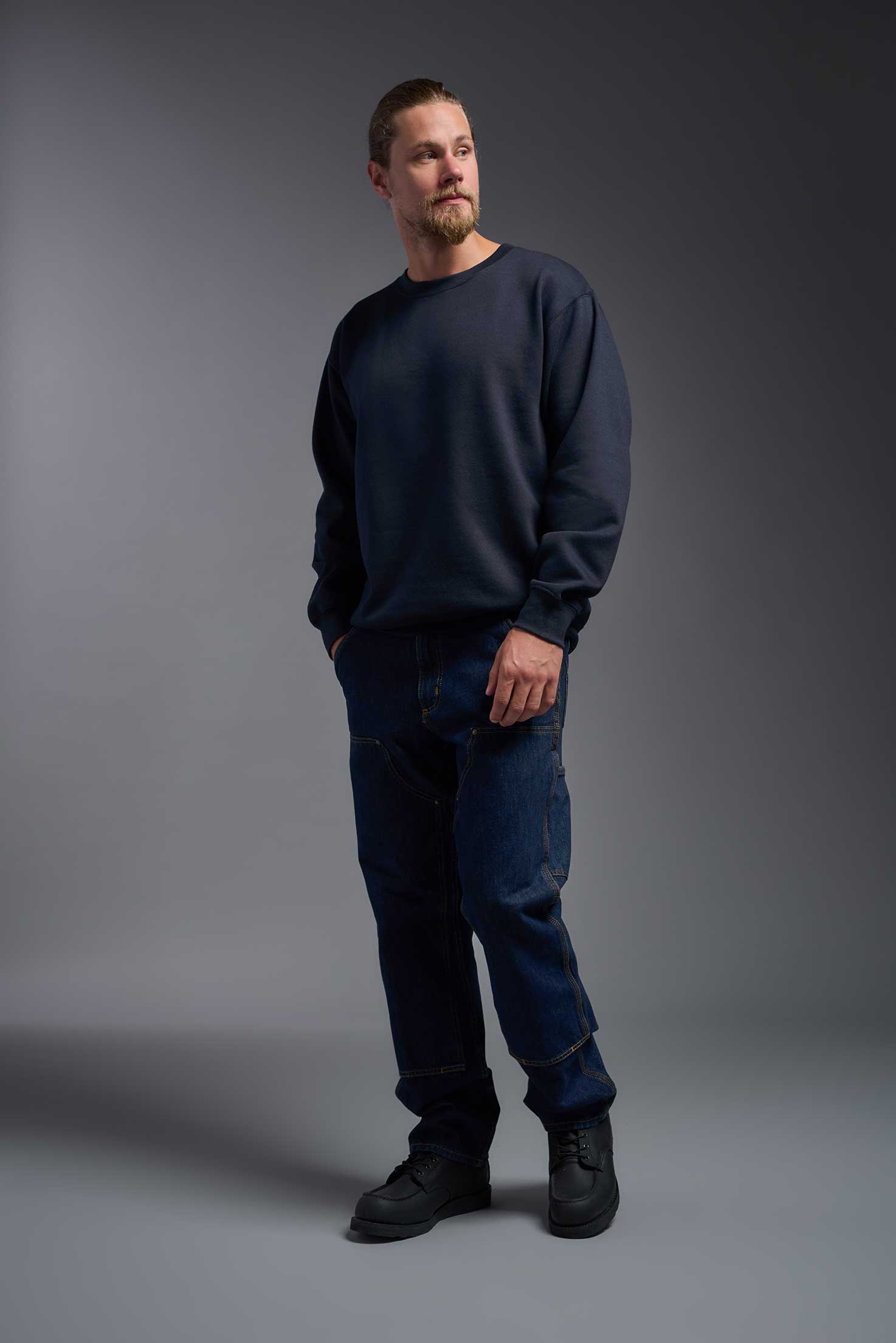 A male model wearing the unisex Americana 3-End Fleece Crewneck Sweatshirt in the color navy, made from 75% combed ring-spun USA-grown cotton and 25% polyester, showing the relaxed fit from a side view. This premium fleece hoodie is Made in the USA. #navy