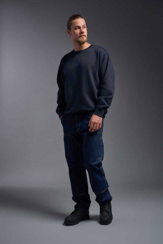 A male model wearing the unisex Americana 3-End Fleece Crewneck Sweatshirt in the color navy, made from 75% combed ring-spun USA-grown cotton and 25% polyester, showing the relaxed fit from a side view. This premium fleece hoodie is Made in the USA. #navy