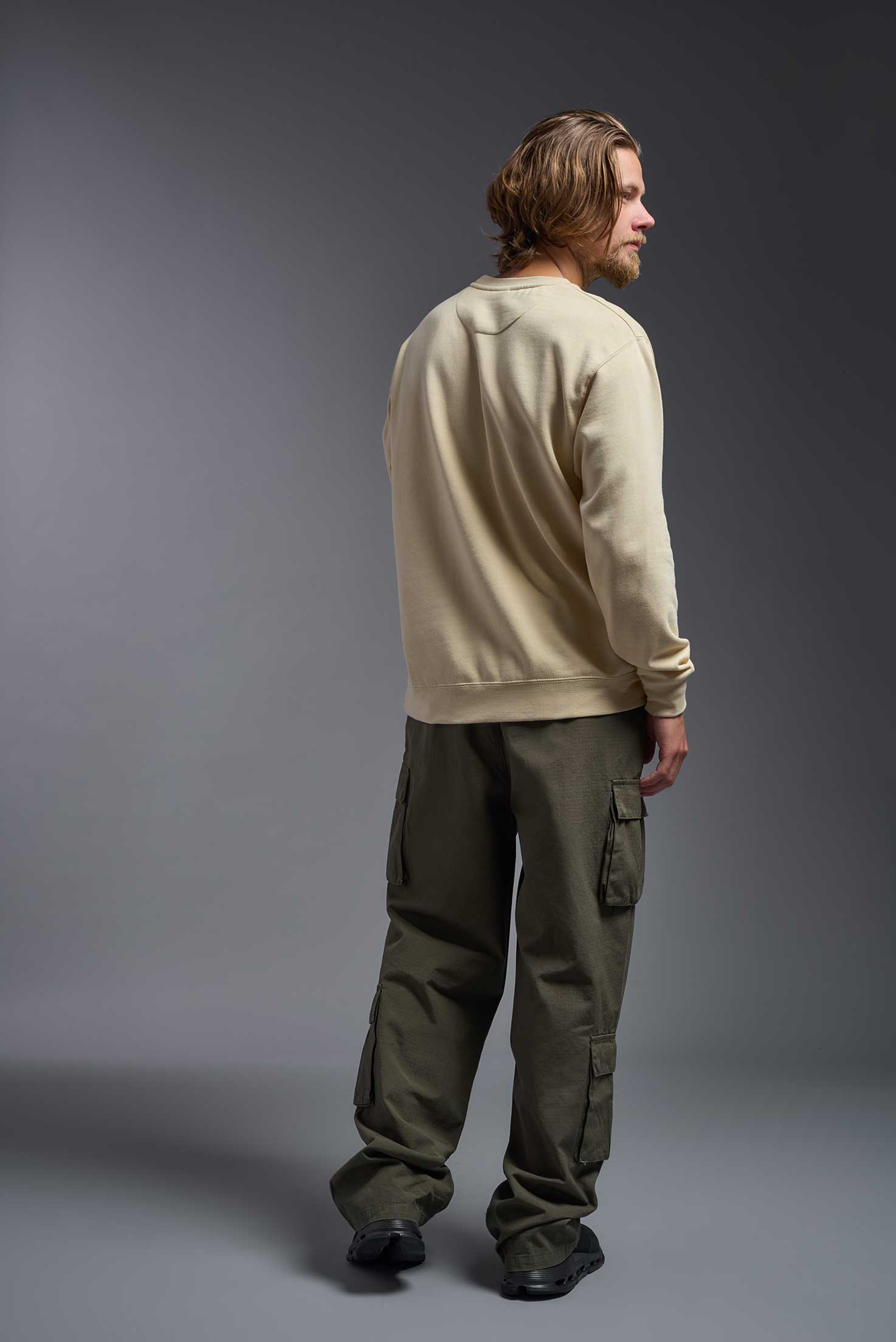 A male model wearing the unisex Americana 3-End Fleece Crewneck Sweatshirt in the color sand, made from 75% combed ring-spun USA-grown cotton and 25% polyester, showing the relaxed fit from a back view. This premium fleece hoodie is Made in the USA. #sand