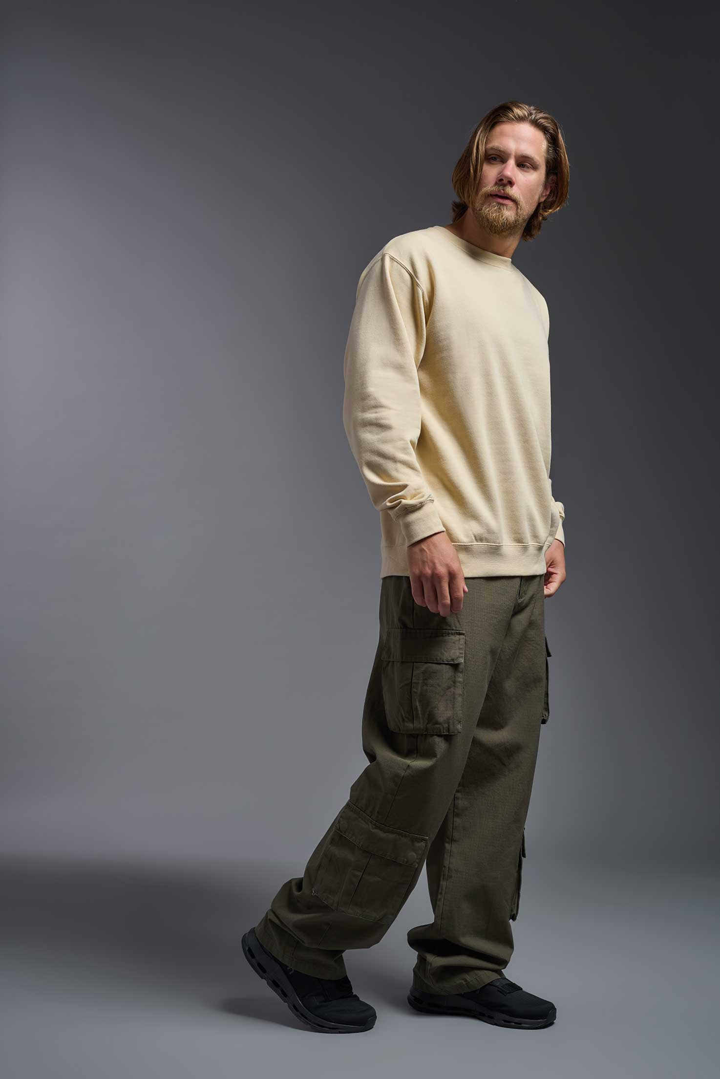 A male model wearing the unisex Americana 3-End Fleece Crewneck Sweatshirt in the color sand, made from 75% combed ring-spun USA-grown cotton and 25% polyester, showing the relaxed fit from a side view. This premium fleece hoodie is Made in the USA. #sand