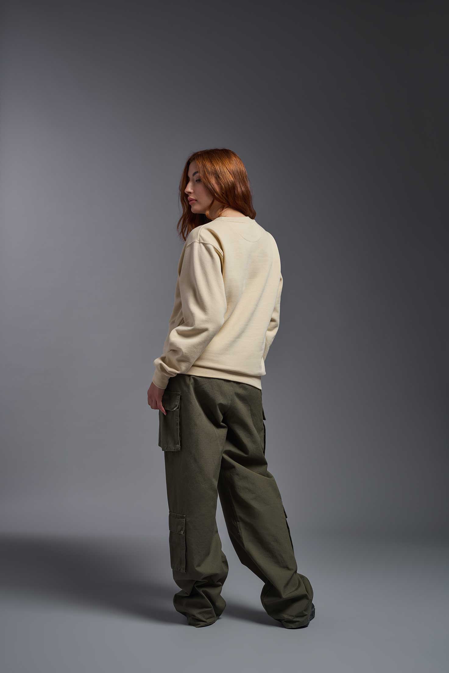A female model wearing the unisex Americana 3-End Fleece Crewneck Sweatshirt in the color sand, made from 75% combed ring-spun USA-grown cotton and 25% polyester, showing the relaxed fit from a back view. This premium fleece hoodie is Made in the USA. #sand