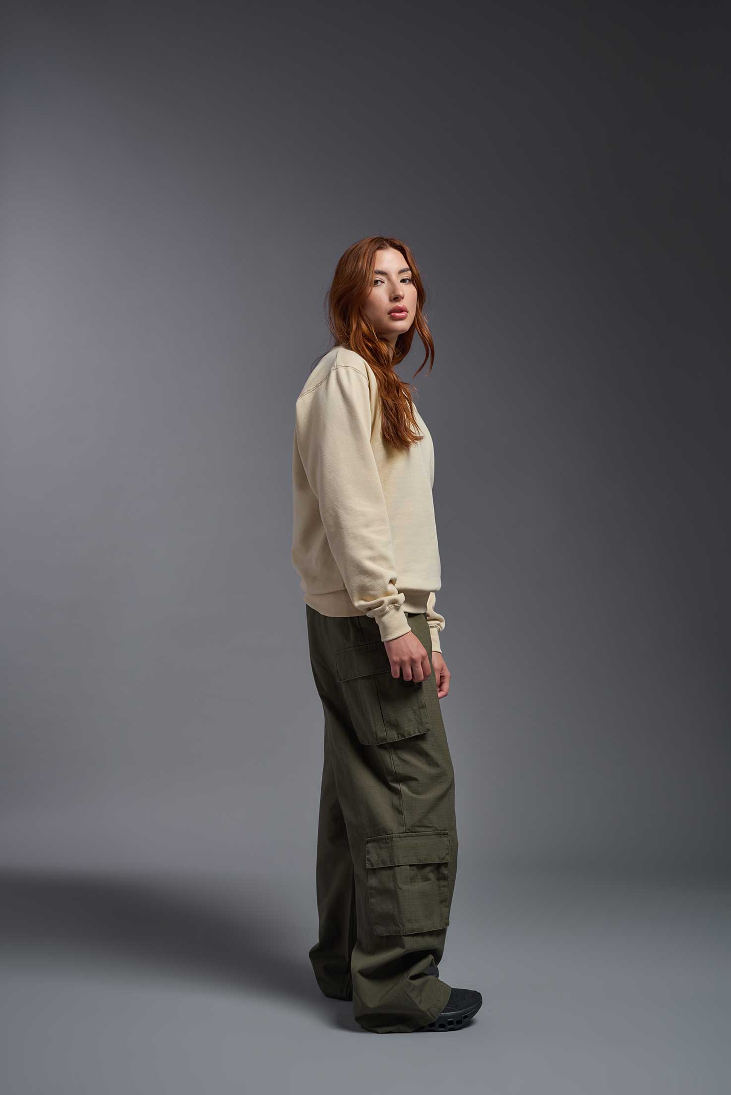 A female model wearing the unisex Americana 3-End Fleece Crewneck Sweatshirt in the color sand, made from 75% combed ring-spun USA-grown cotton and 25% polyester, showing the relaxed fit from a side view. This premium fleece hoodie is Made in the USA. #sand