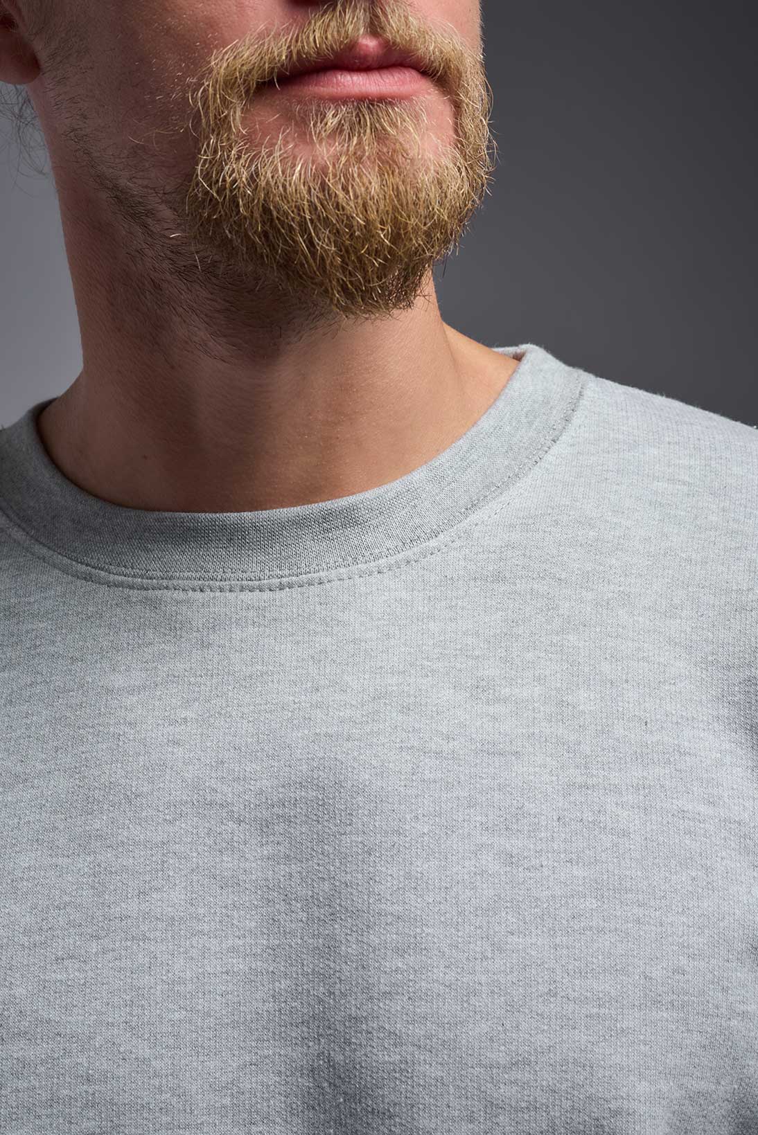 A male model wearing the unisex Americana 3-End Fleece Crewneck Sweatshirt in the color sport gray, made from 75% combed ring-spun USA-grown cotton and 25% polyester, showing the relaxed fit from a close-up view of the collar. This premium fleece hoodie is Made in the USA. #sport-gray