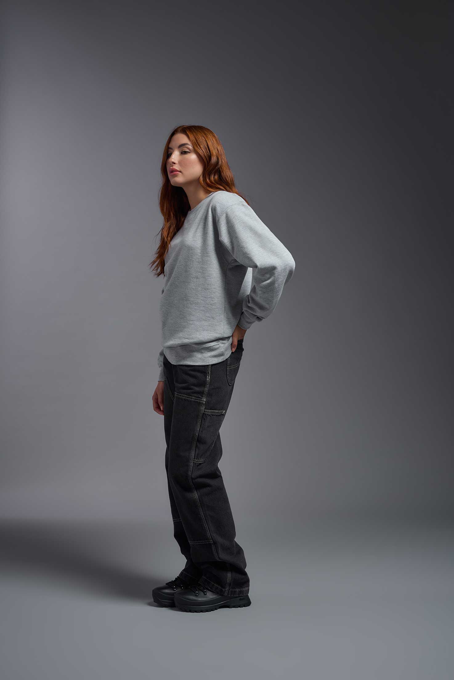 A female model wearing the unisex Americana 3-End Fleece Crewneck Sweatshirt in the color sport gray, made from 75% combed ring-spun USA-grown cotton and 25% polyester, showing the relaxed fit from a side view. This premium fleece hoodie is Made in the USA. #sport-gray