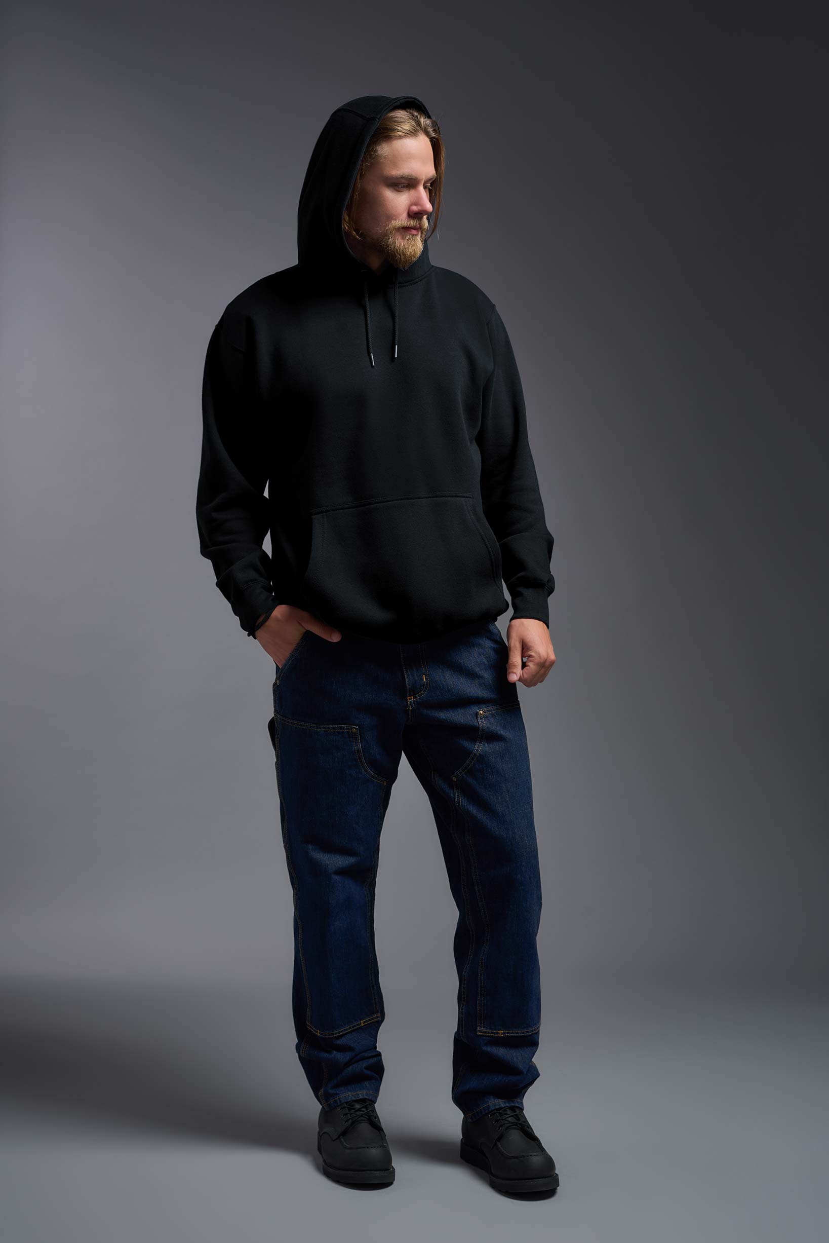 A male model wearing the unisex Americana 3-End Fleece Pullover Hoodie in the color black, made from 75% combed ring-spun USA-grown cotton and 25% polyester, showing the relaxed fit from a front view with hood up. This premium fleece hoodie is Made in the USA. #black