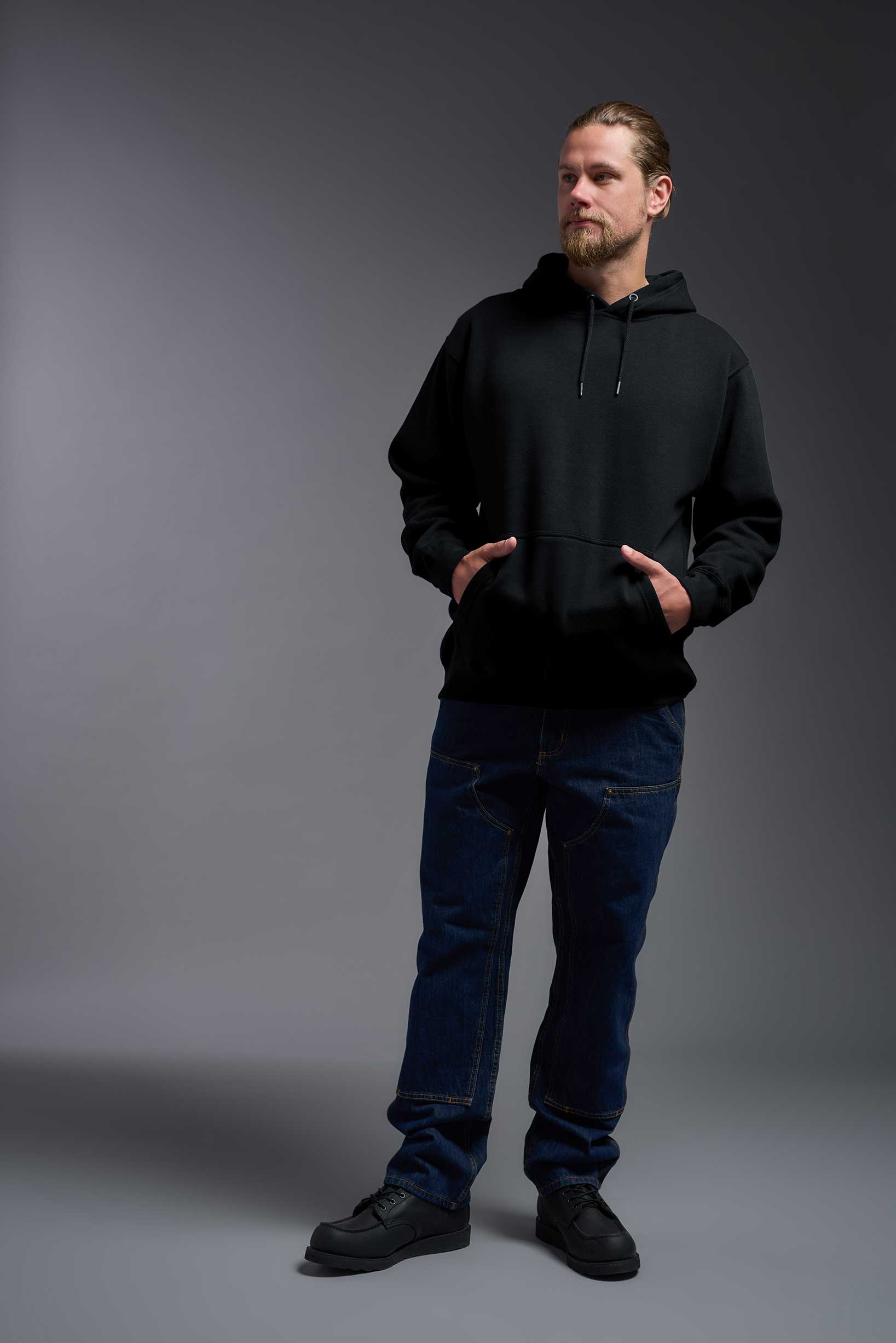 A male model wearing the unisex Americana 3-End Fleece Pullover Hoodie in the color black, made from 75% combed ring-spun USA-grown cotton and 25% polyester, showing the relaxed fit from a front view. This premium fleece hoodie is Made in the USA. #black