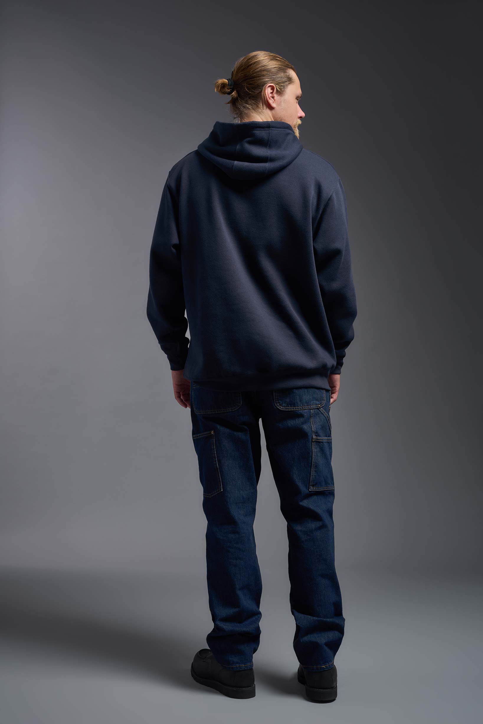 A male model wearing the unisex Americana 3-End Fleece Pullover Hoodie in the color navy, made from 75% combed ring-spun USA-grown cotton and 25% polyester, showing the relaxed fit from a back view. This premium fleece hoodie is Made in the USA. #navy