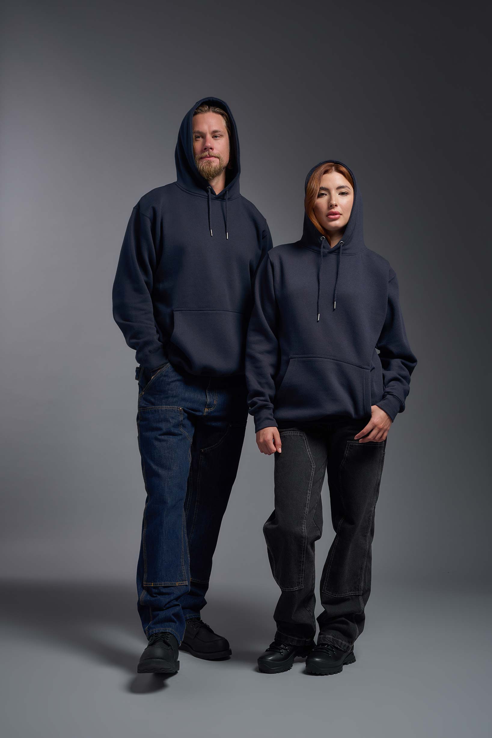 A male and female model wearing the unisex Americana 3-End Fleece Pullover Hoodie in the color navy, made from 75% combed ring-spun USA-grown cotton and 25% polyester, showing the relaxed fit from a front view with hoods up. This premium fleece hoodie is Made in the USA. #navy